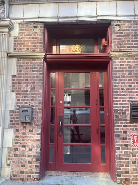 Brick building entrance with a maroon glass door and stone trim.