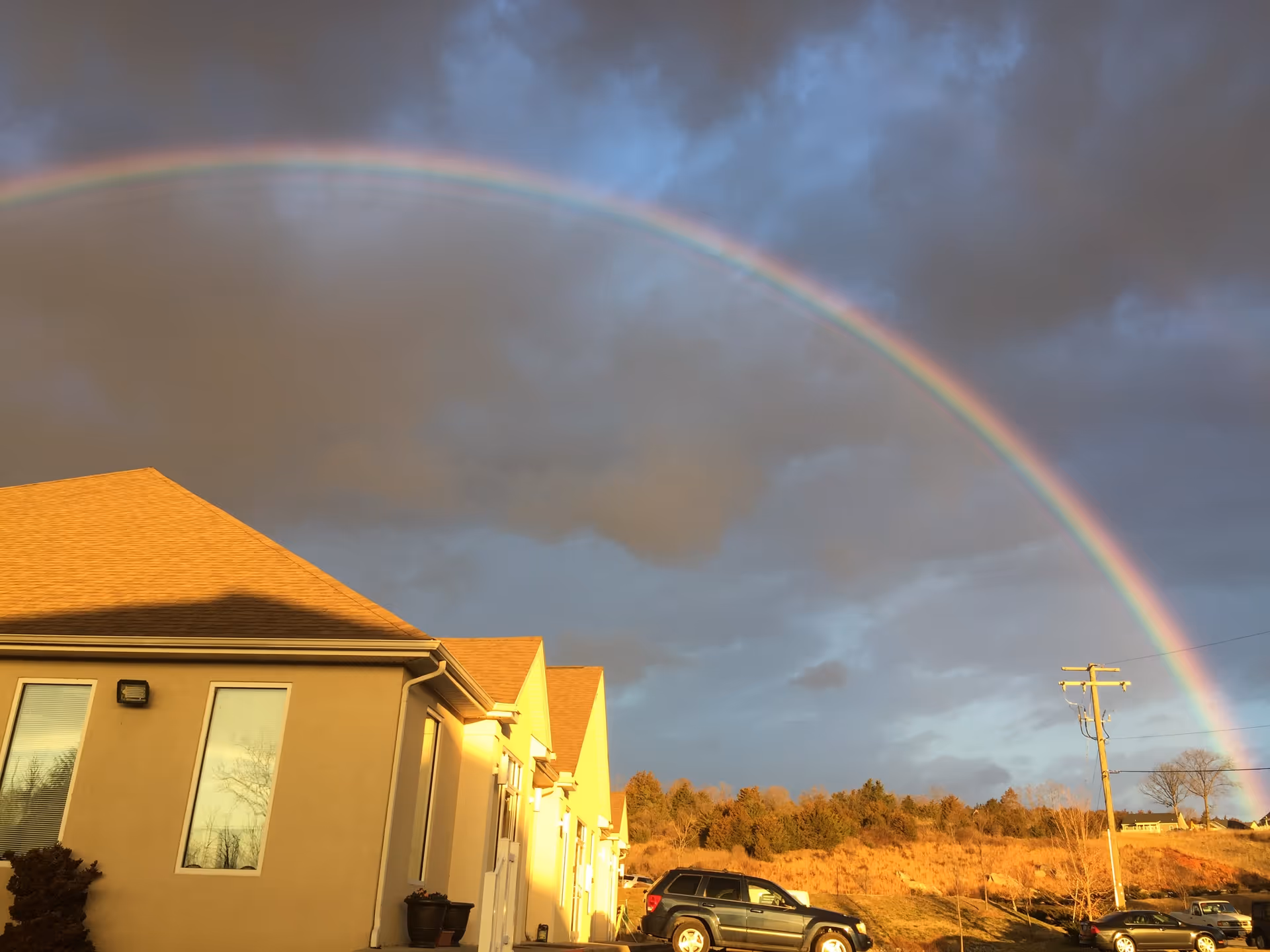 Front of a beige senior facility with a vivid rainbow across a cloudy sky.