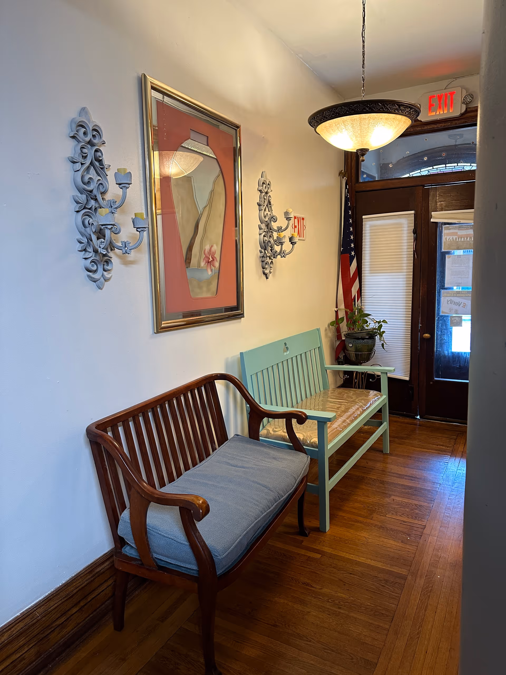 Interior hallway seating with wooden bench, aqua chair, wall art, and exit door.
