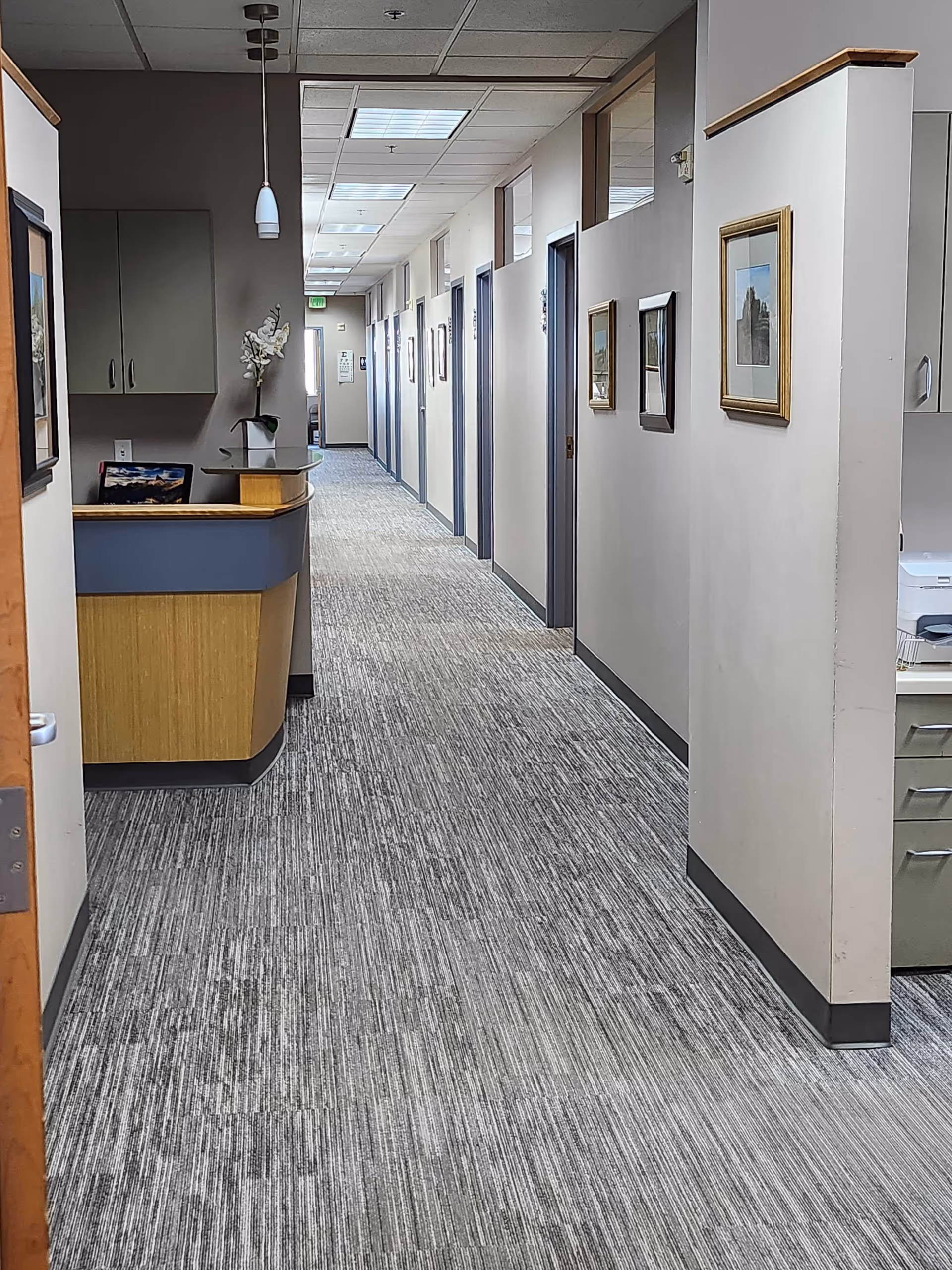 Long hallway in a facility with reception desk, framed art, and multiple doors along walls.