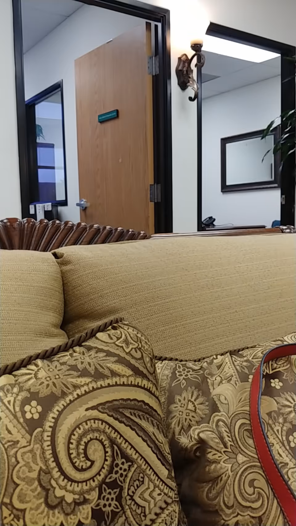Cushioned patterned sofa dominates a lobby area with a wooden door and wall mirror.