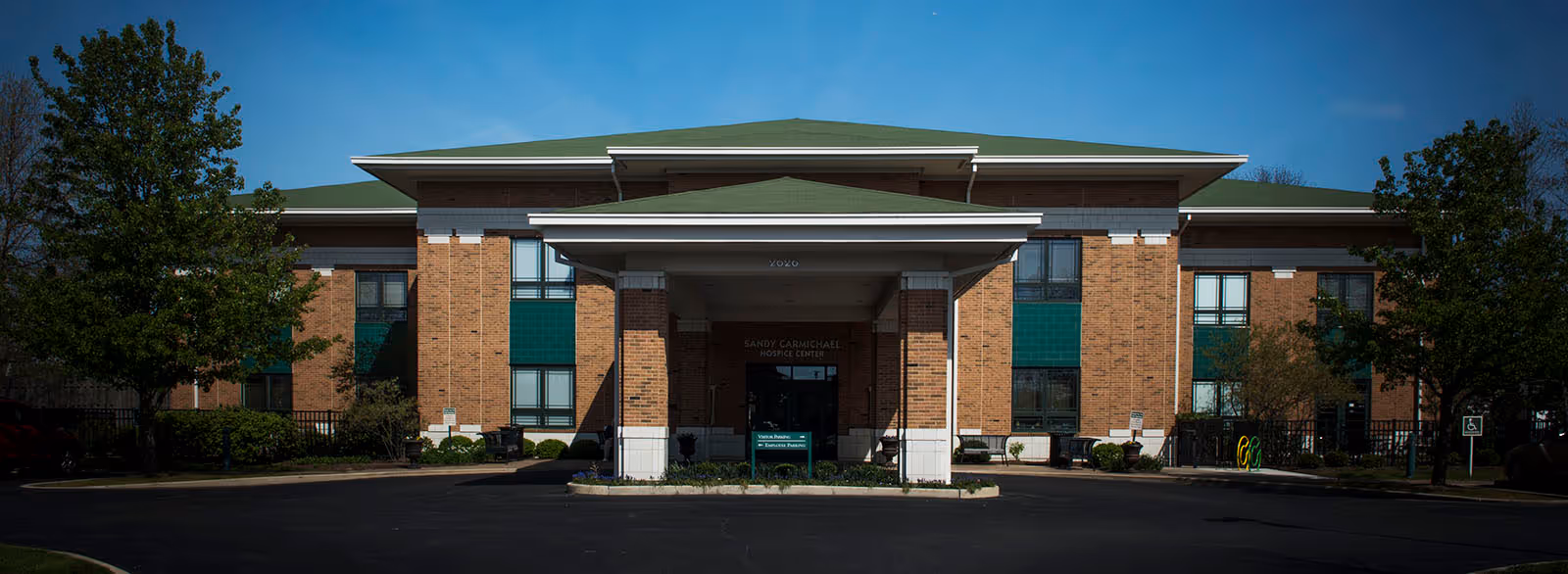 Brick hospice facility with a covered front entrance and green roof accents.