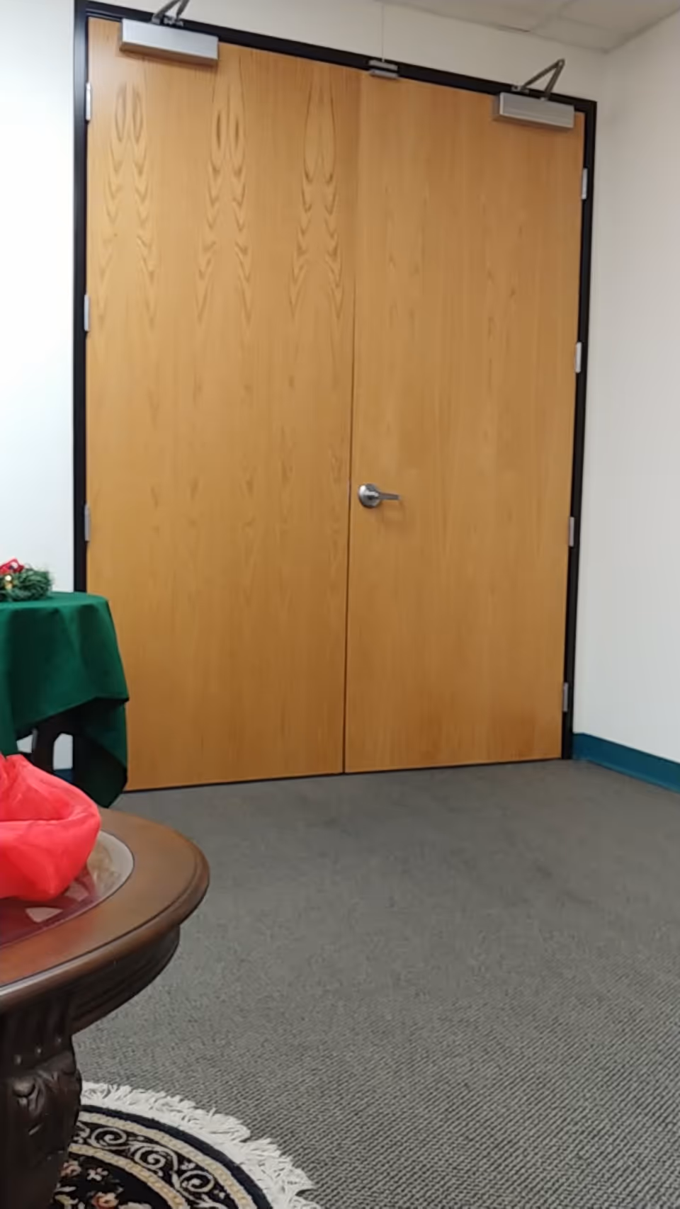 Double wooden doors dominate a plain interior hallway with a round table nearby.