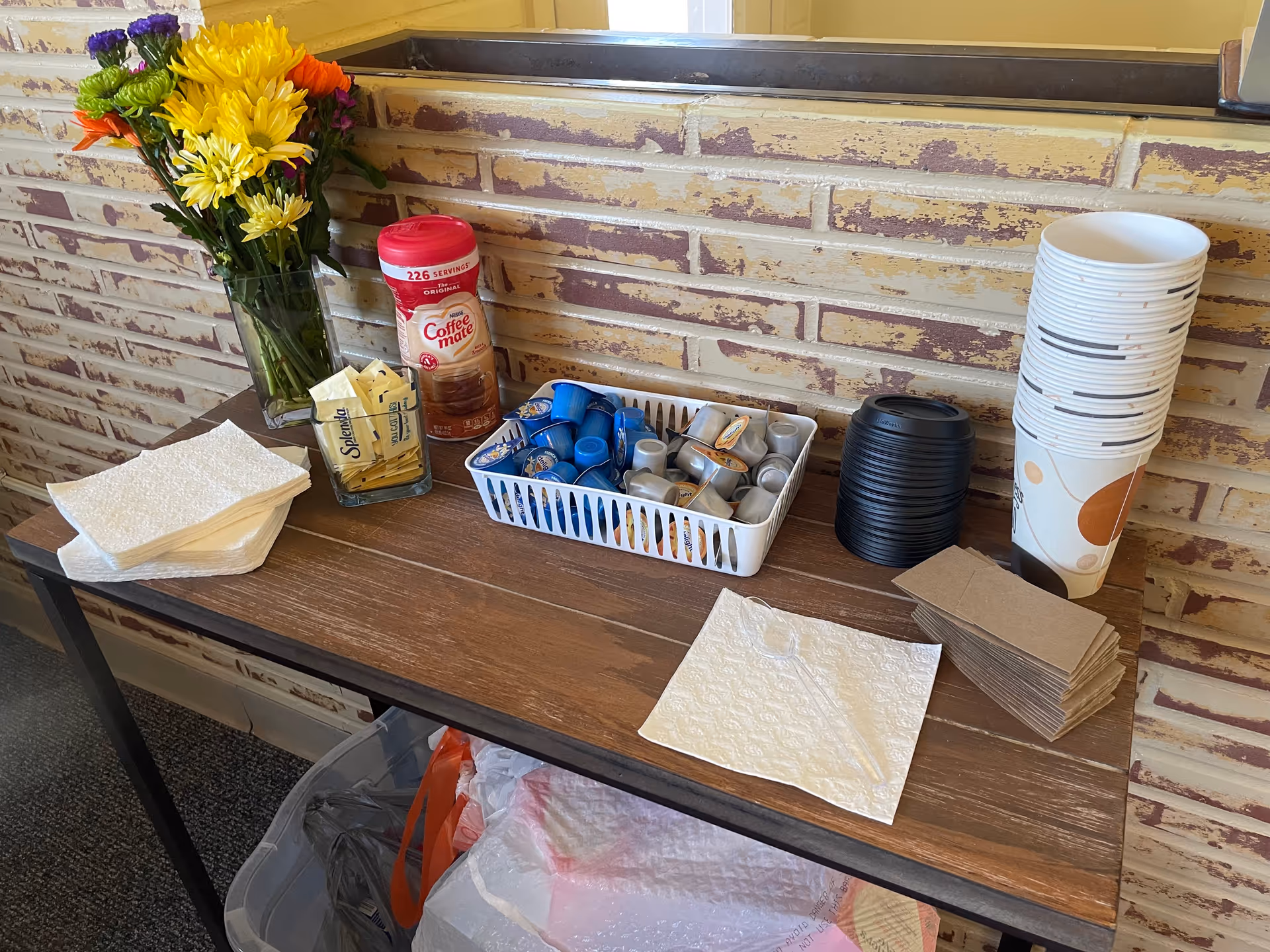Coffee station on a wooden table with cups, creamers, napkins, and flowers.