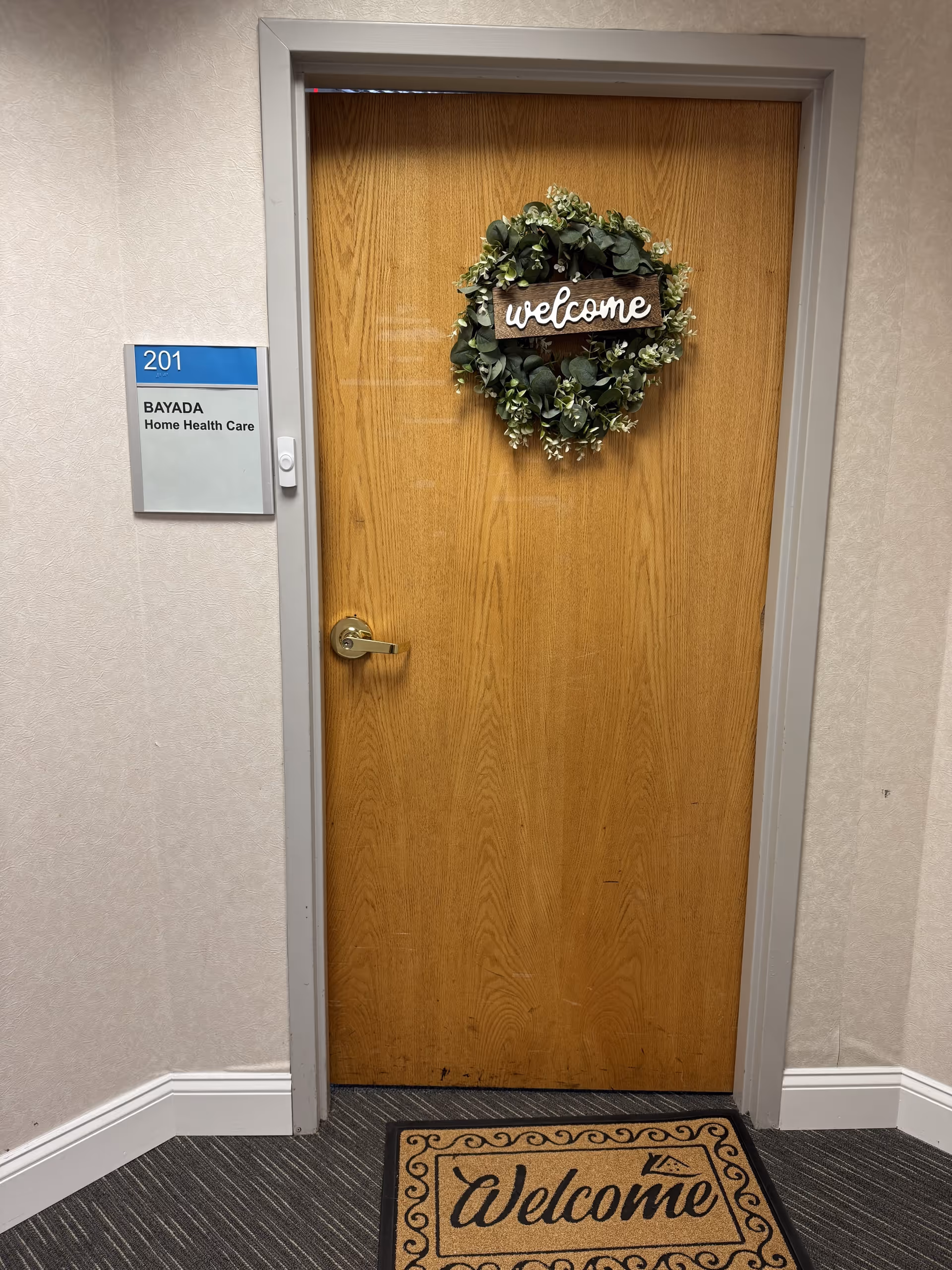 Wooden interior door with wreath reading 'welcome' beside a BAYADA sign in a hallway.