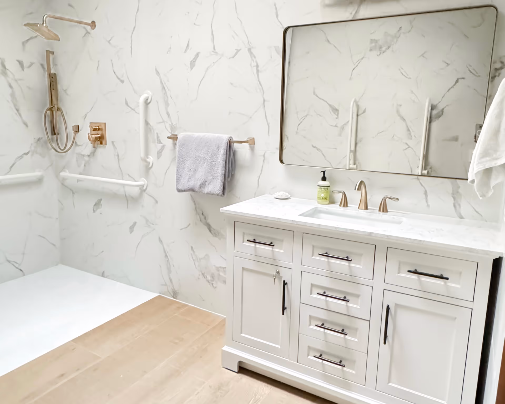 Modern marble bathroom with vanity, sink, mirror, towel bars, and accessibility grab bars.