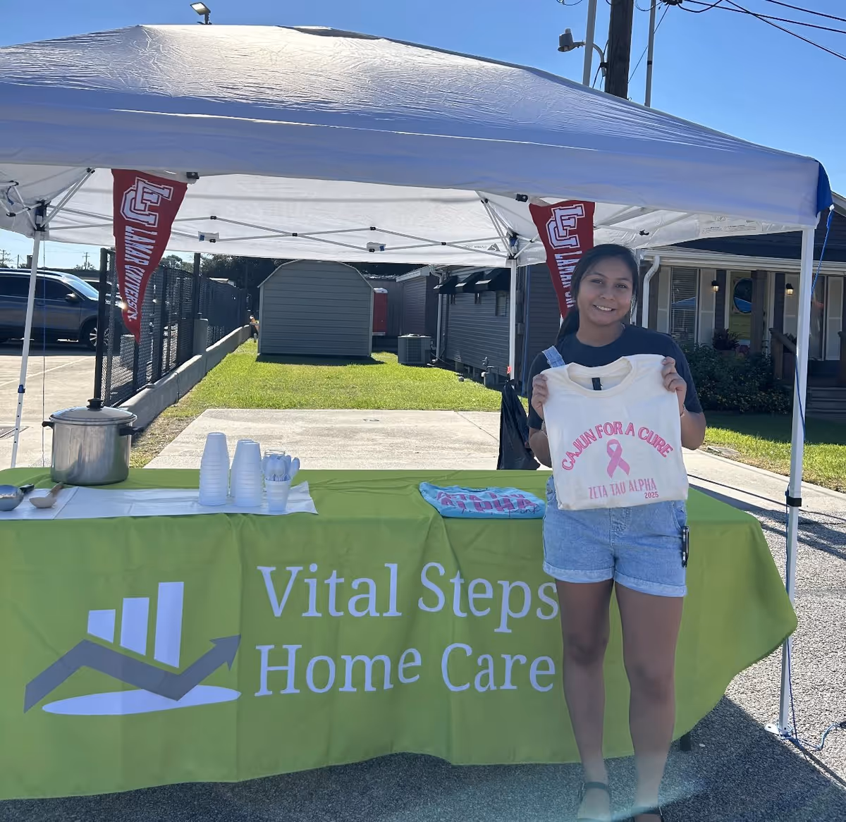 Outdoor tent setup for Vital Steps Home Care with a smiling person holding a tote bag.