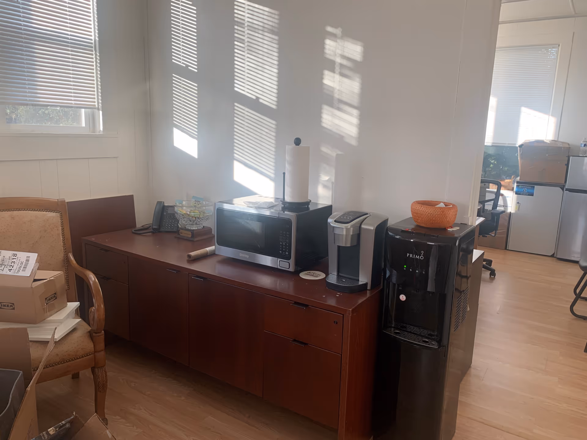 Wooden cabinet with microwave, coffee maker, paper towel, and boxes in a small kitchen area.