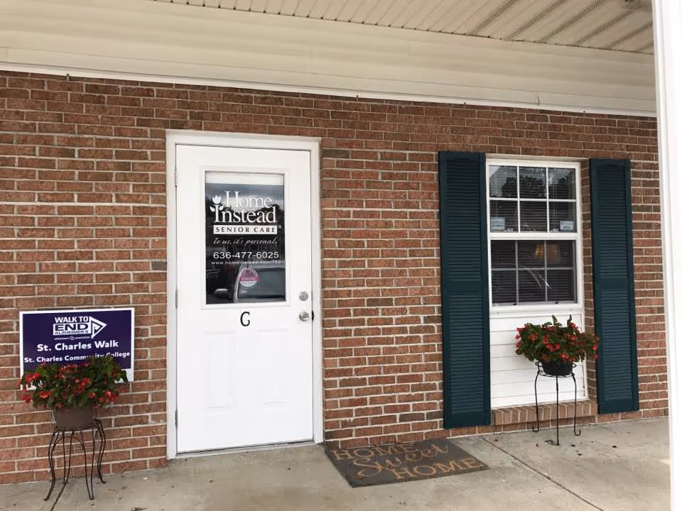 Brick building exterior featuring a white door marked Home Instead and a window with shutters.
