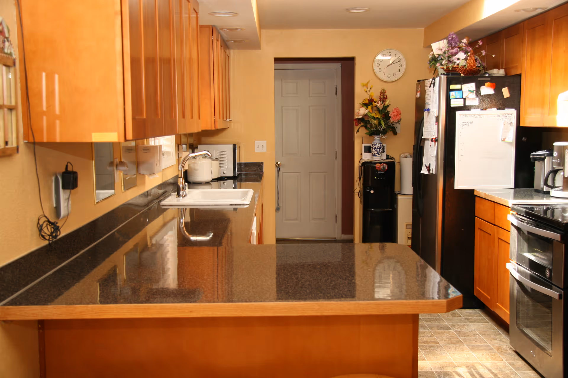 Long kitchen with granite countertops, wooden cabinets, sink, and stainless appliances.