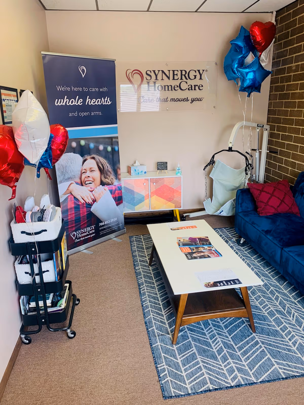 Synergy HomeCare welcome area with banners, balloons, a couch, and a coffee table.