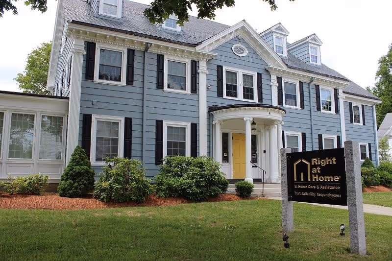 Blue two-story house exterior with a white-trimmed entrance and Right at Home sign.