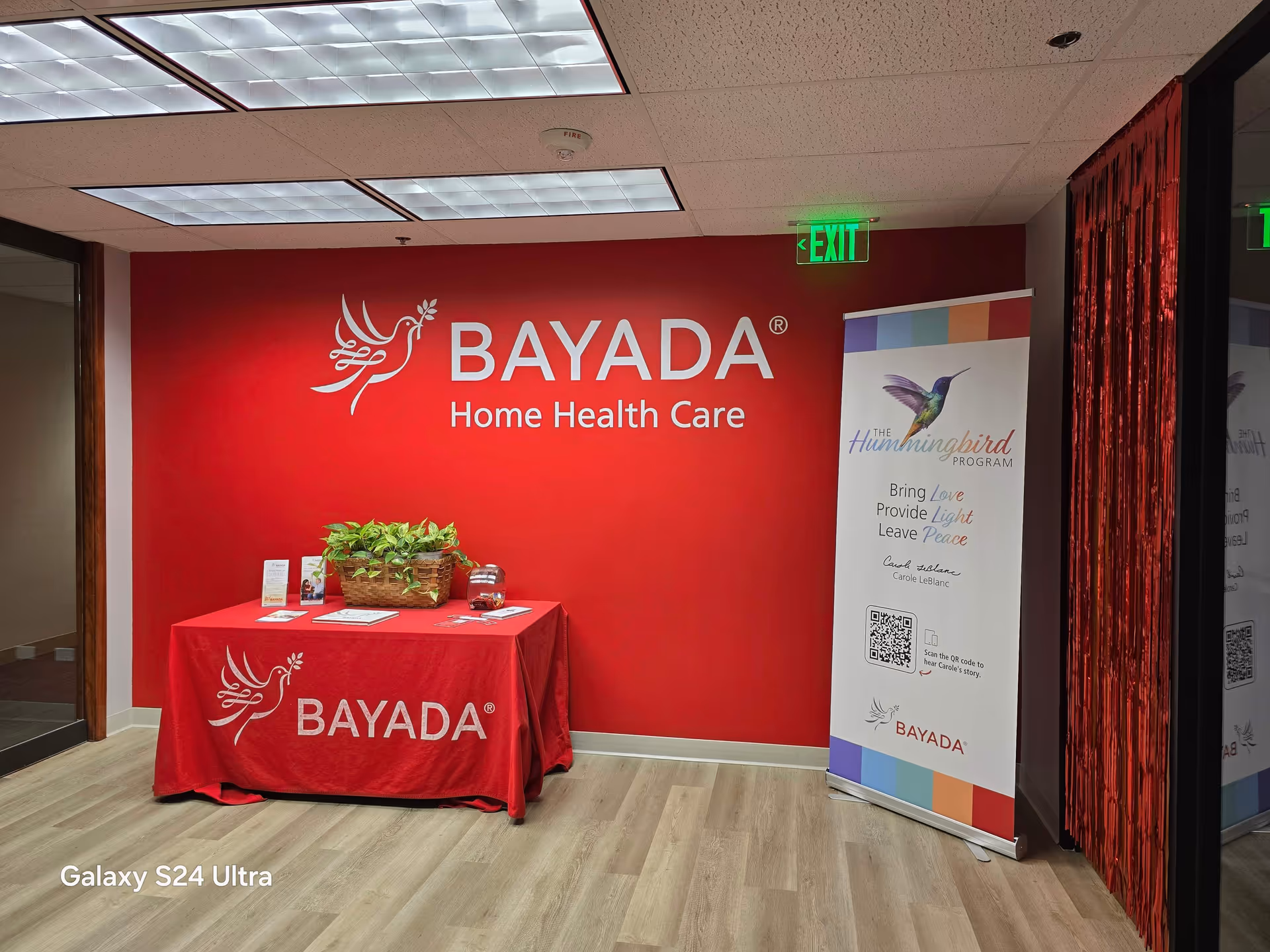 Red BAYADA interior reception area with table, plants, and a display banner.
