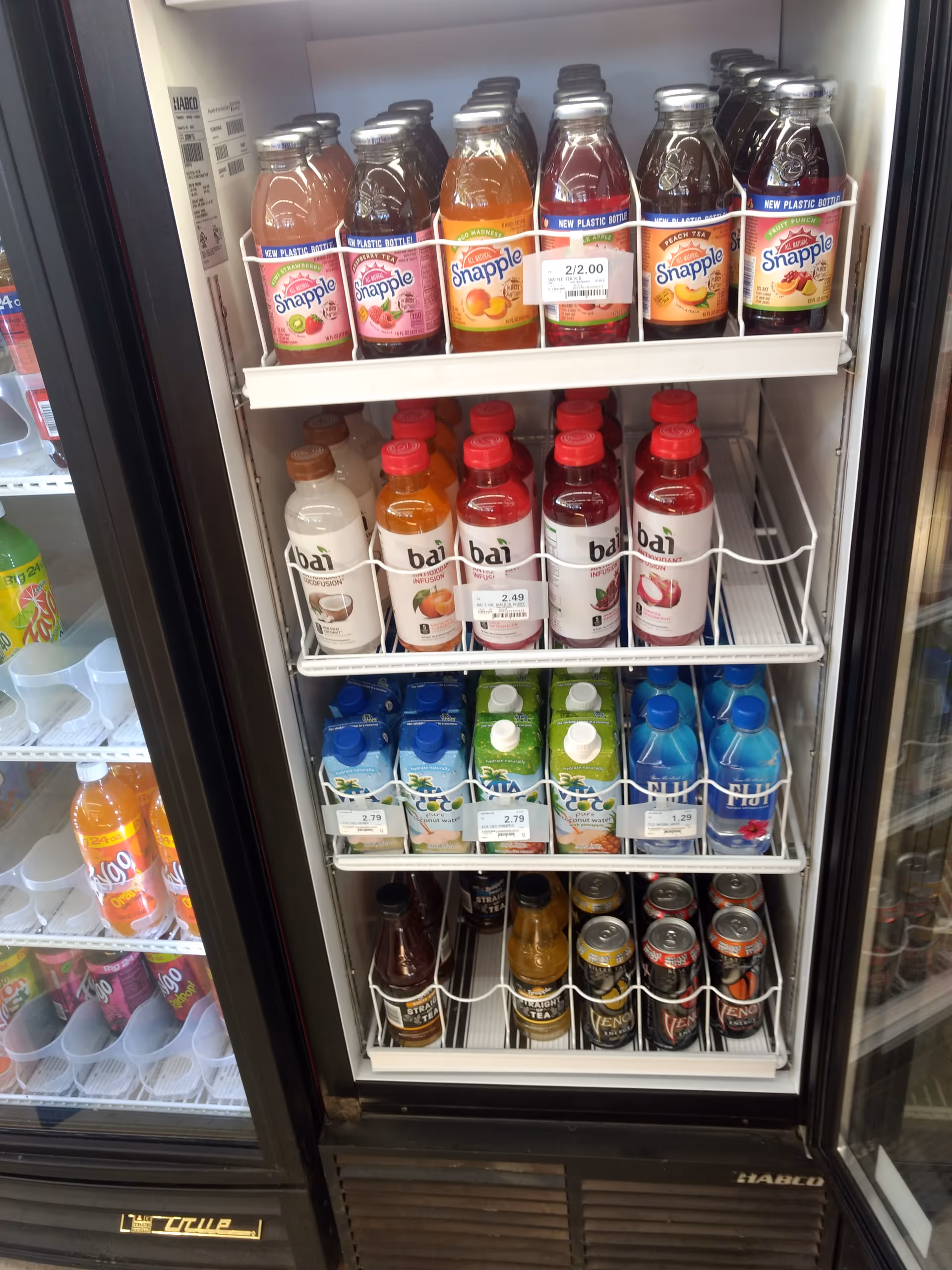 Vertical refrigerated display case with assorted bottled beverages in a store.