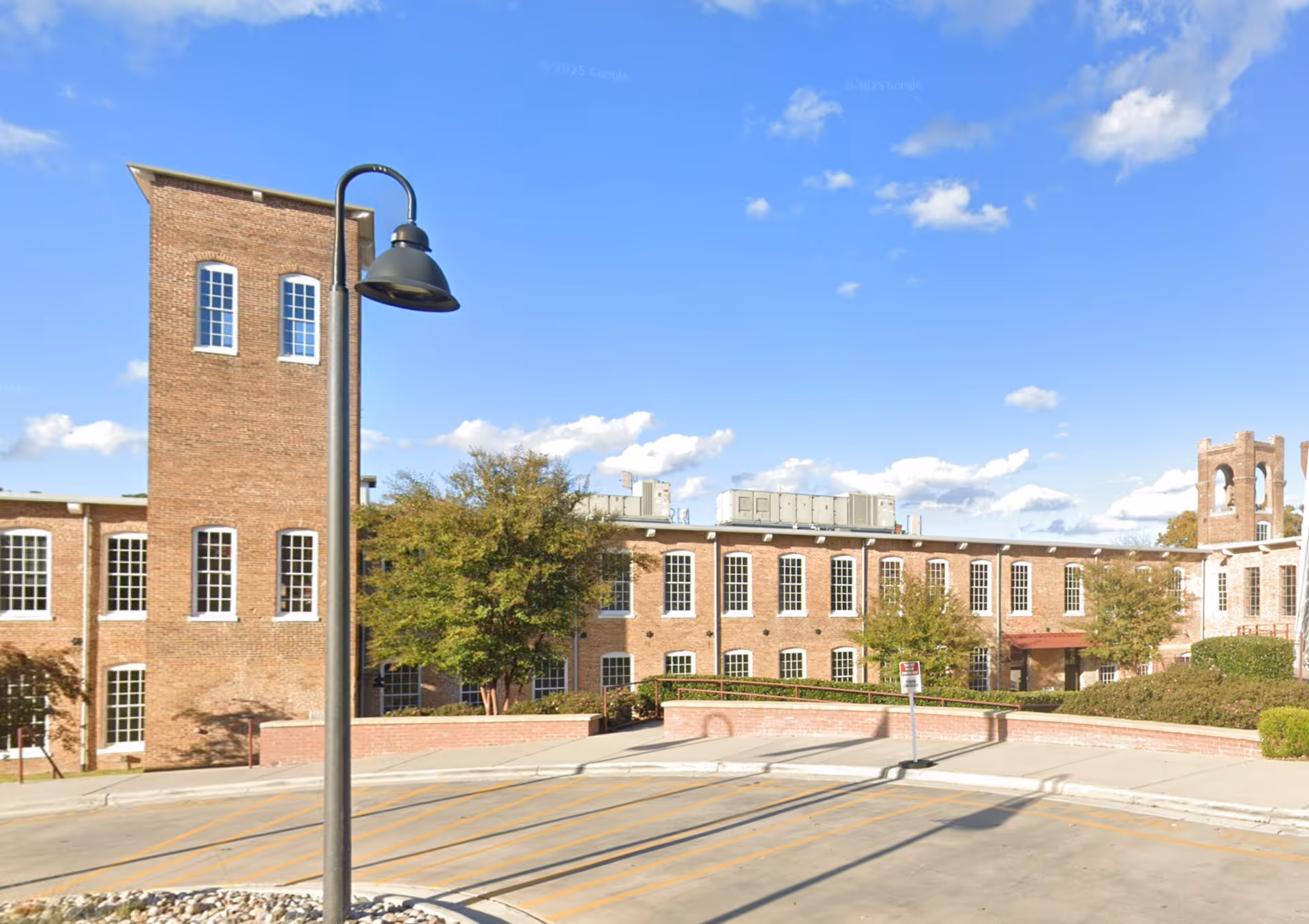 Brick senior living facility exterior with a lamp, trees, and blue sky.