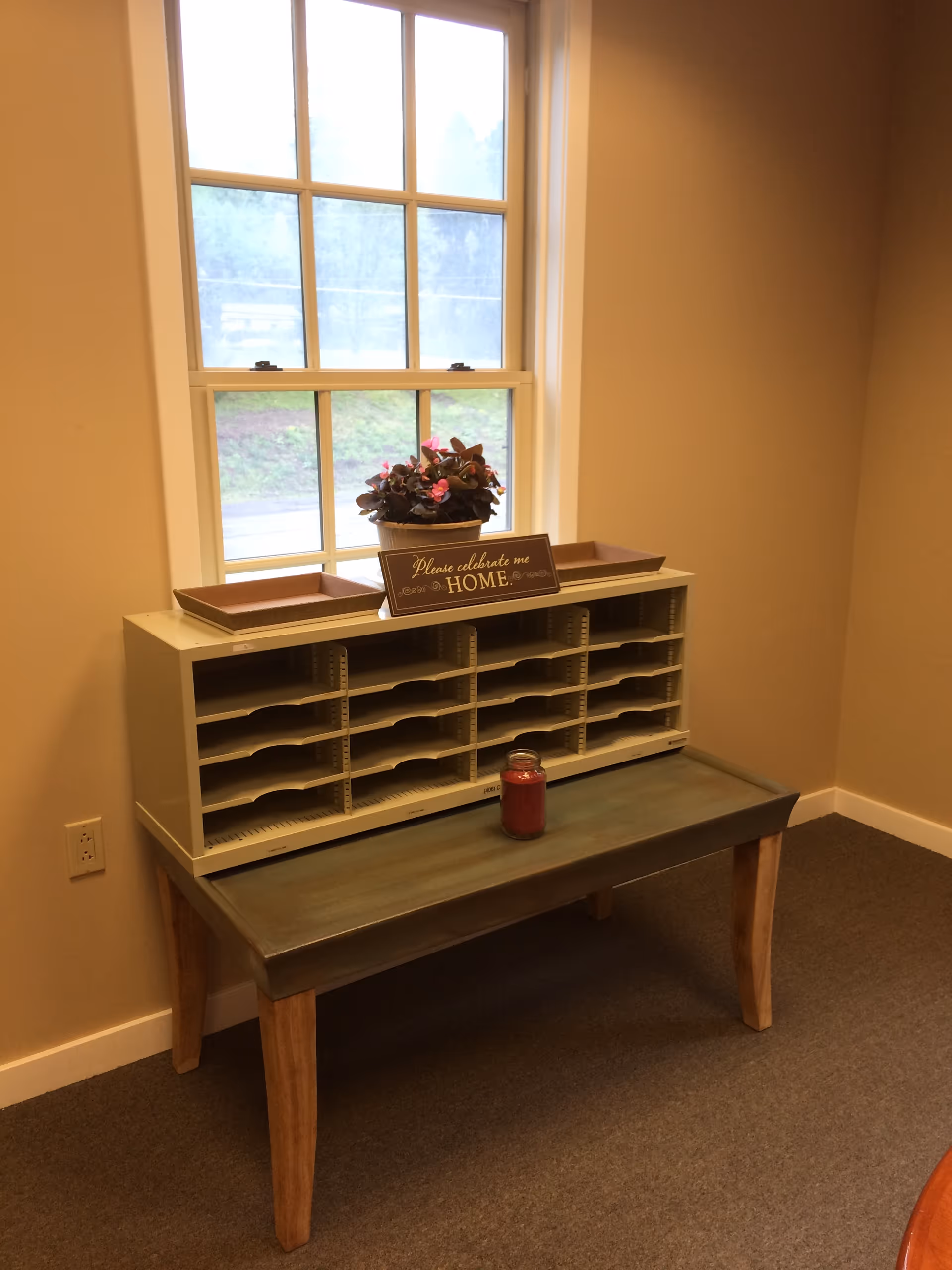 Interior nook with a wooden table, mail sorter, window, and potted flowers.