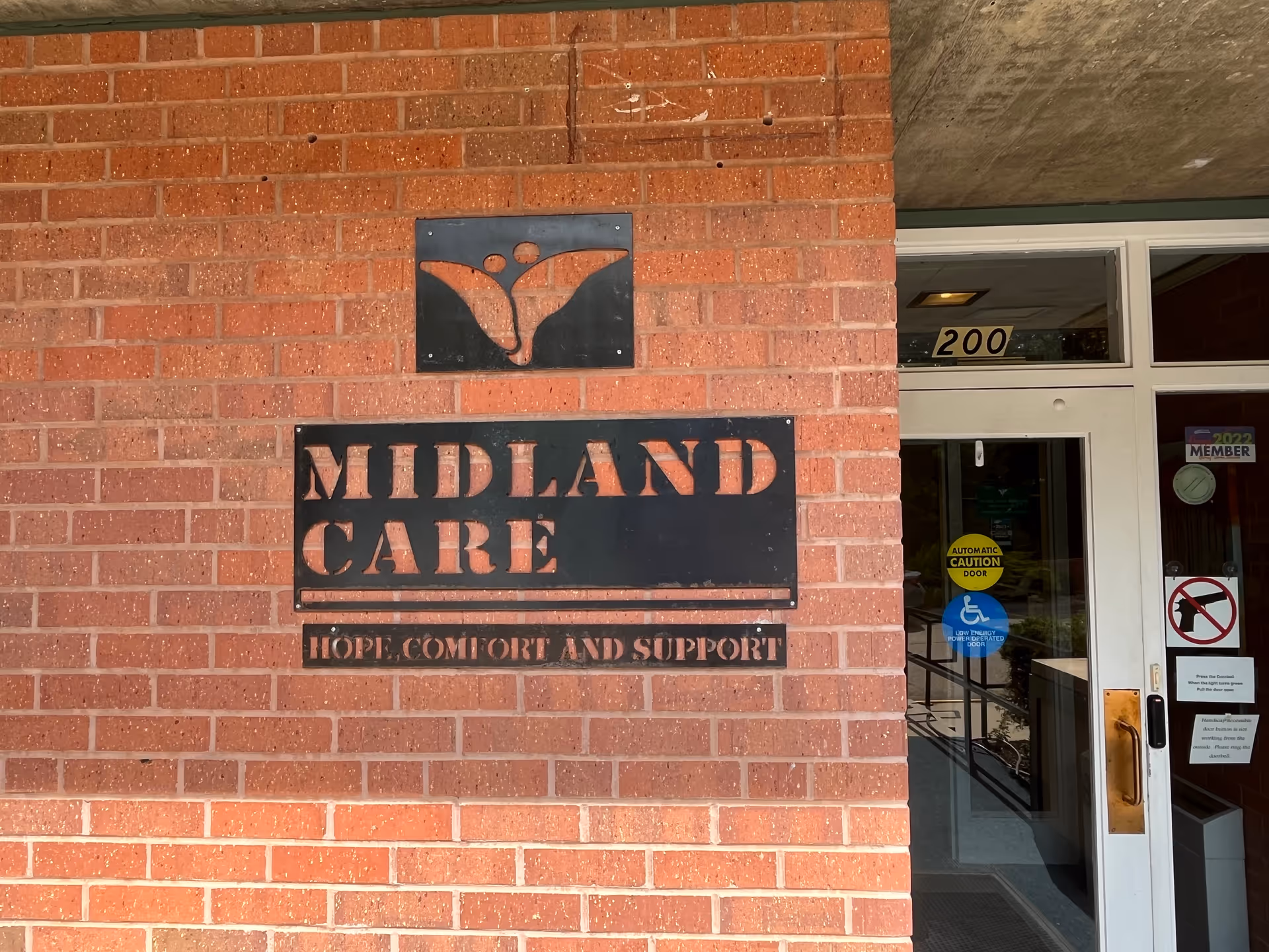 Exterior view of Midland Care entrance on brick wall with sign and glass door.