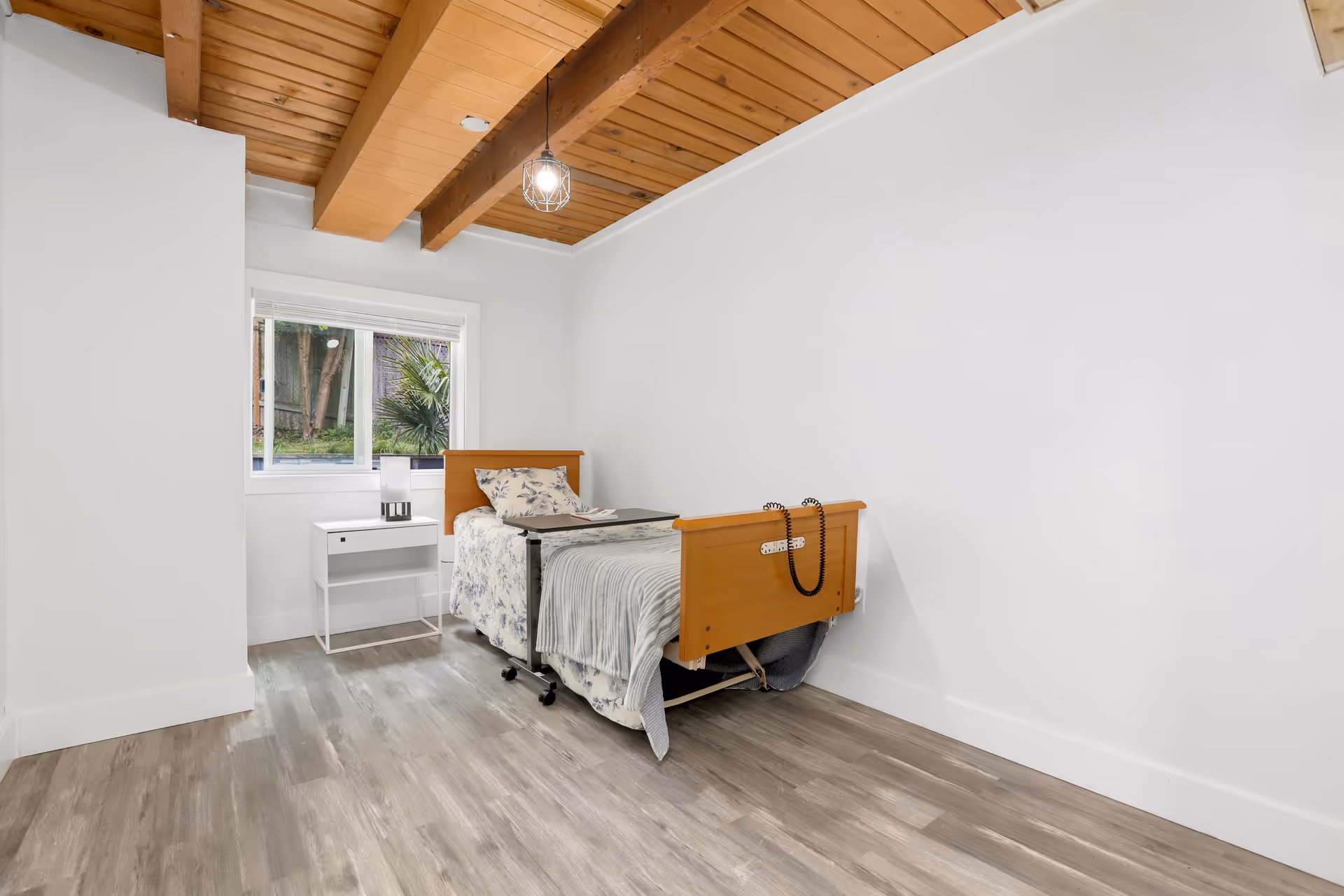 A small bedroom with an adjustable wooden bed, white walls, and a window.