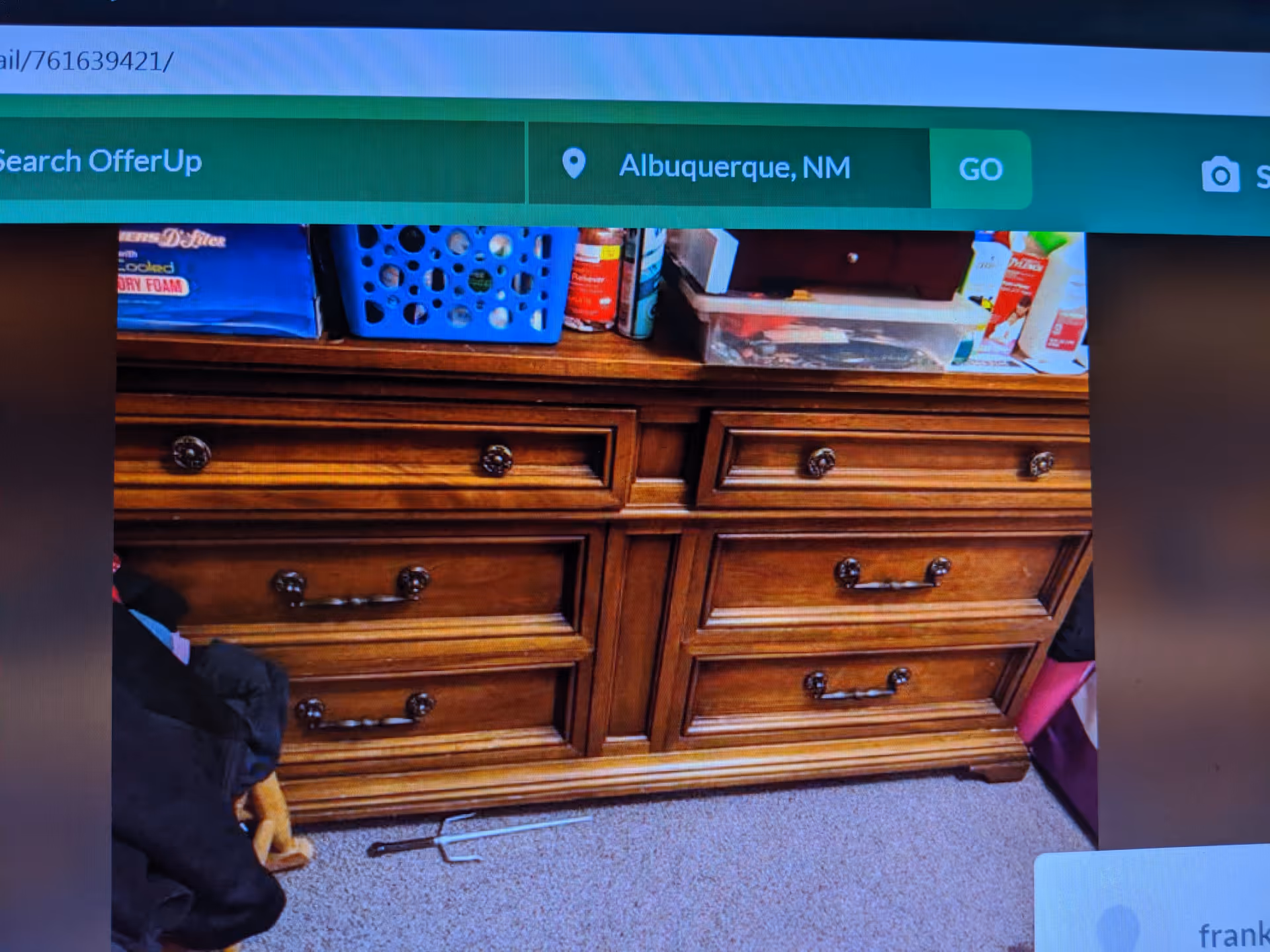 A wooden dresser with multiple drawers and clutter on top in an indoor bedroom.