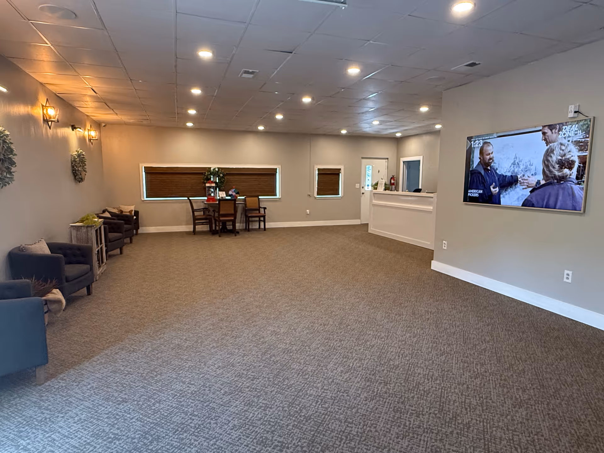 A spacious senior living facility lobby with seating, a reception desk, and a wall-mounted TV.