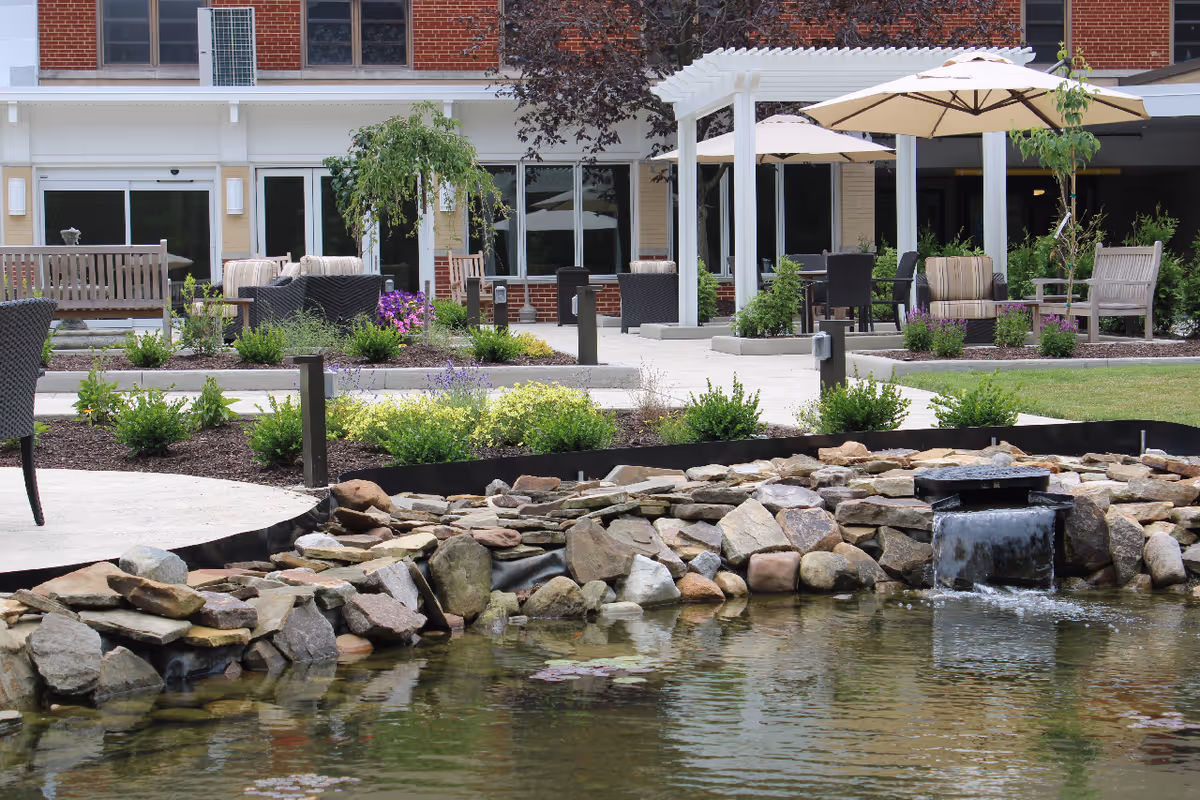 Outdoor courtyard with seating, umbrellas, and a rock waterfall near the facility building.