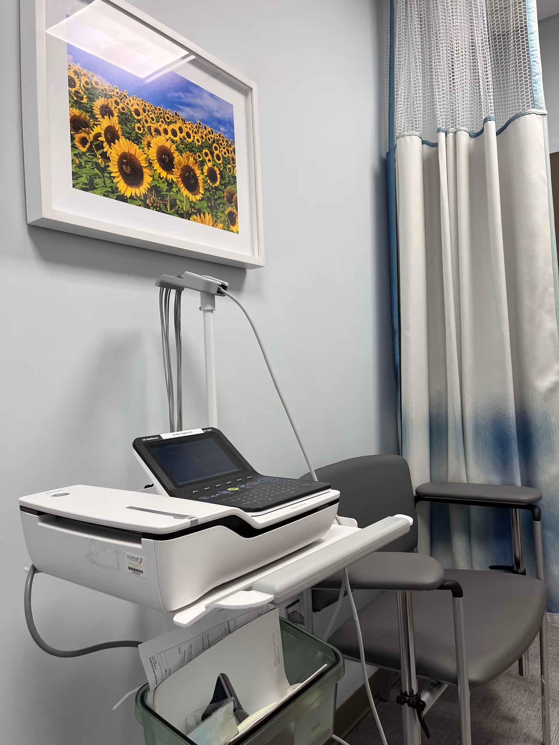 Medical device on a counter beside a chair in a small, curtained examination room.