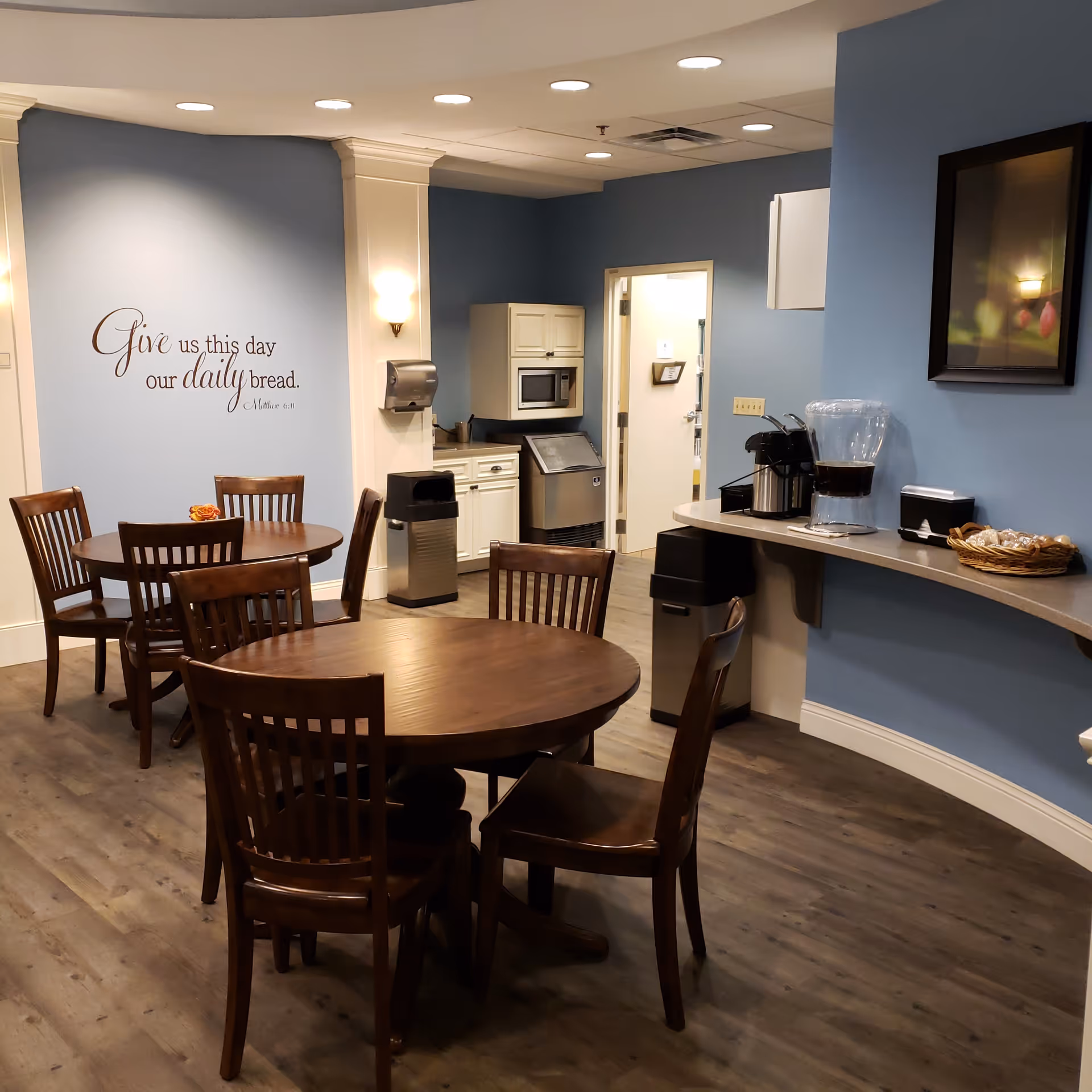 A dining area with round wooden tables, chairs, and a coffee station along blue walls.
