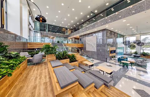 Bright modern senior living lobby with wooden benches, greenery, glass railings, and lounge seating.
