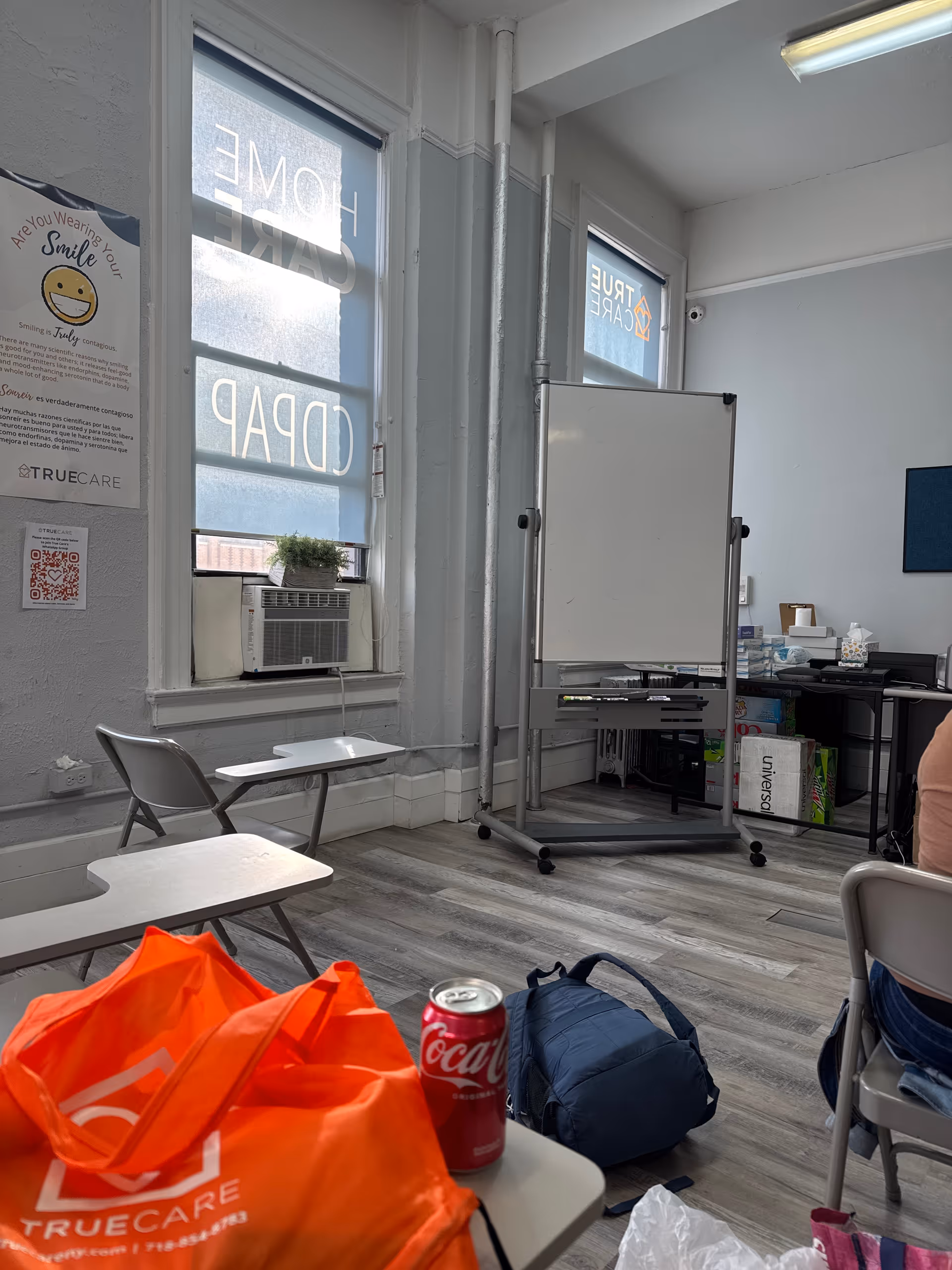Bright facility room with folding desks, a whiteboard, window AC unit, and TrueCare branding.