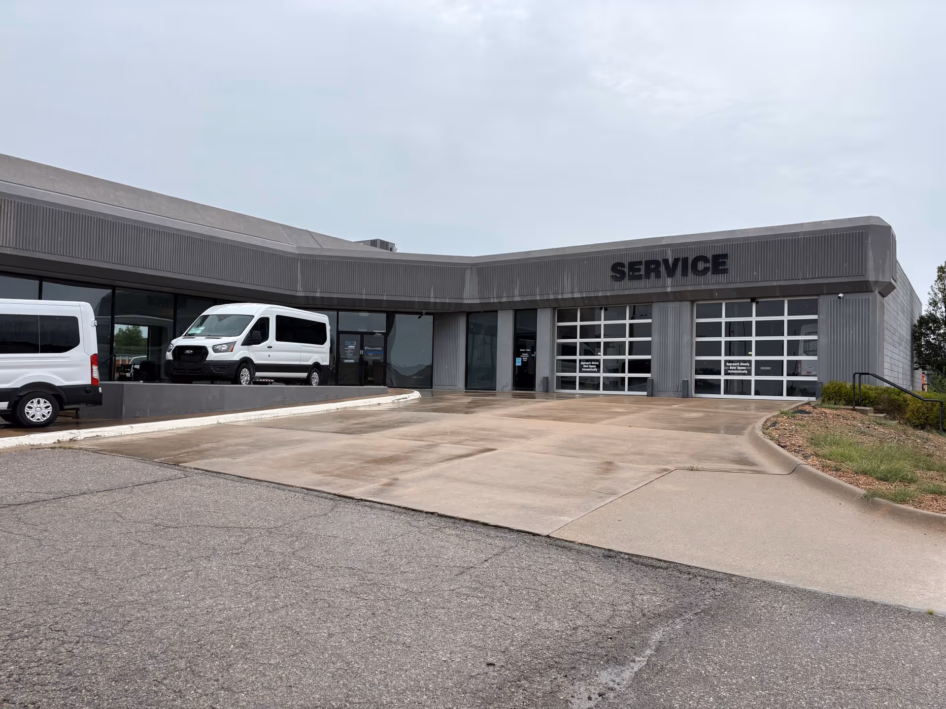 Gray commercial building with 'SERVICE' sign and parked white vans at a sloped front entrance.