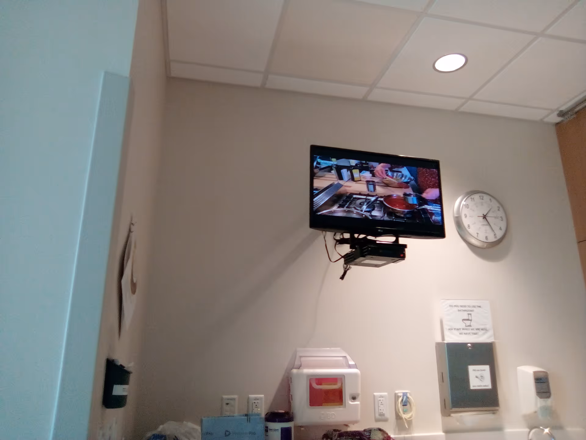 Interior hospital room with wall-mounted monitor, clock, and medical equipment.