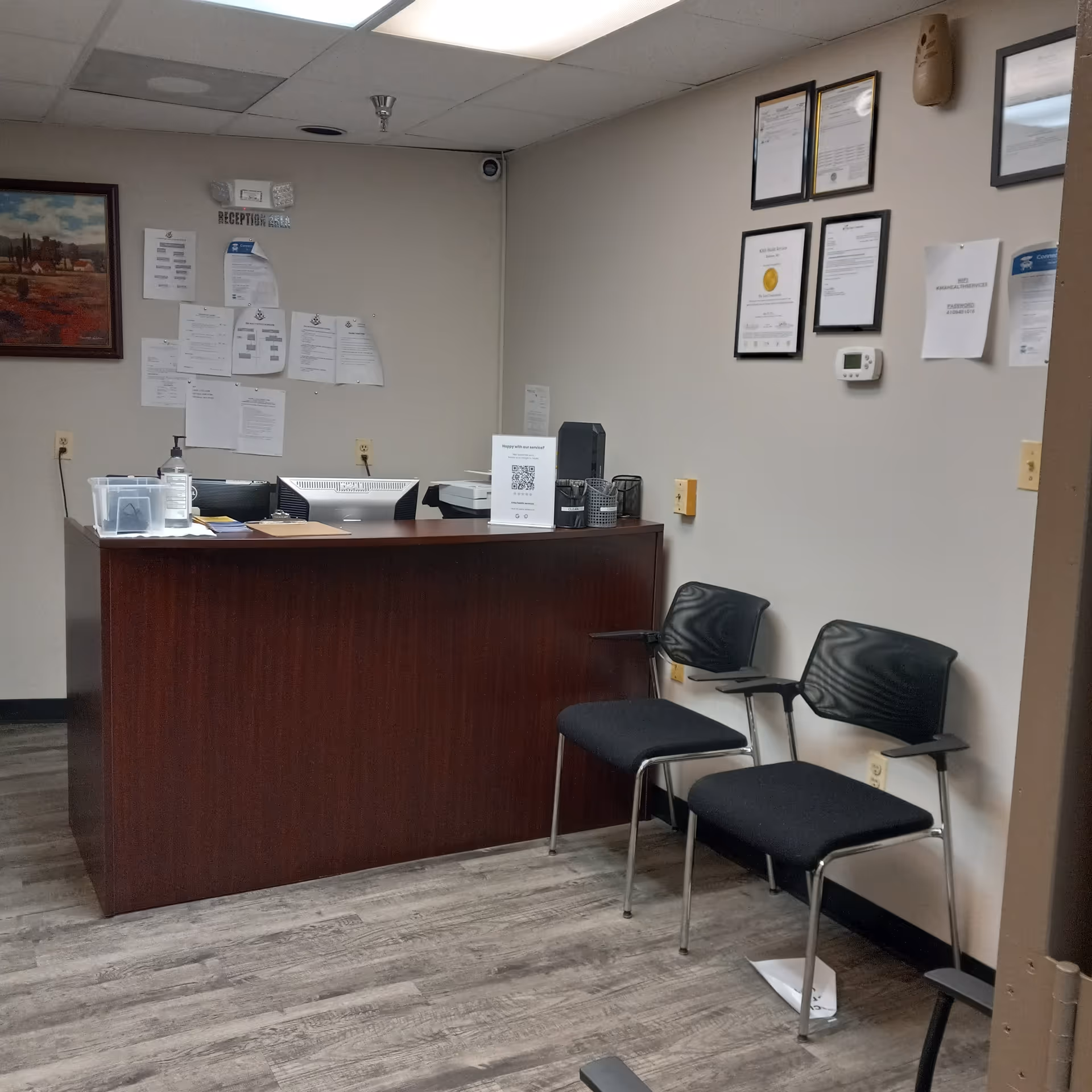 A reception desk in a hallway area with chairs and framed certificates on the wall.