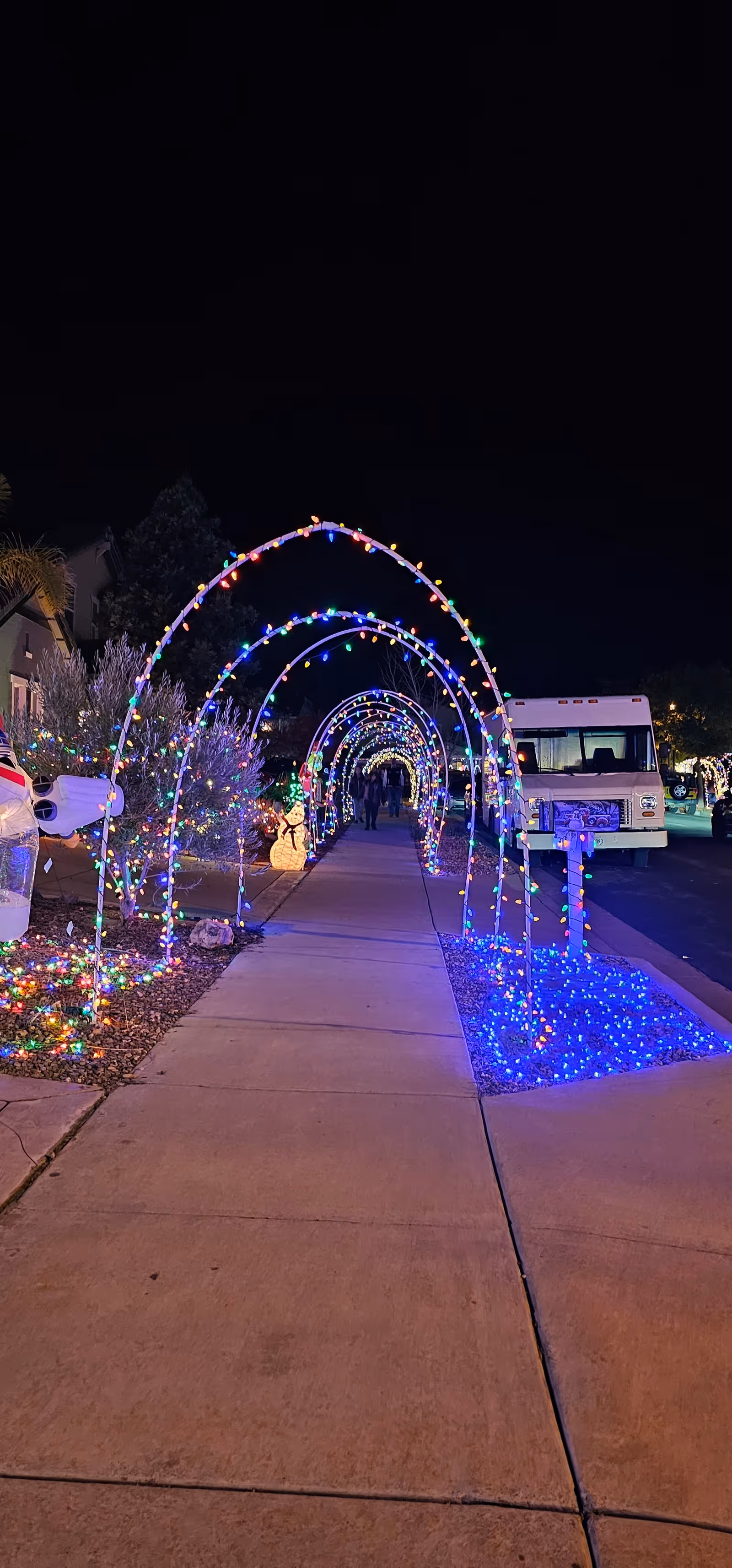 Nighttime outdoor sidewalk with colorful light arches along a facility entrance.