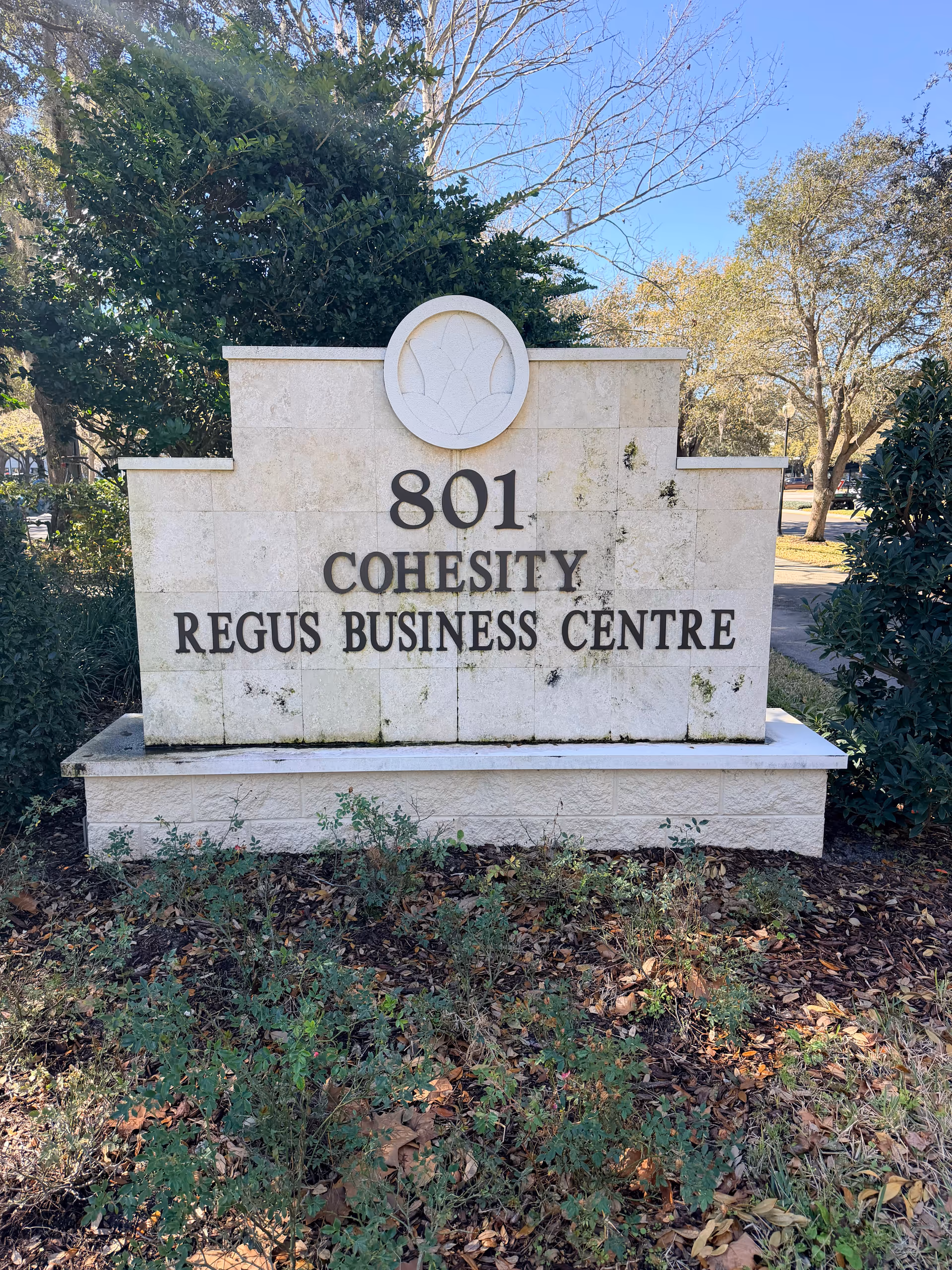 Outdoor stone sign with 801 Cohesity Regus Business Centre, surrounded by trees and shrubs.