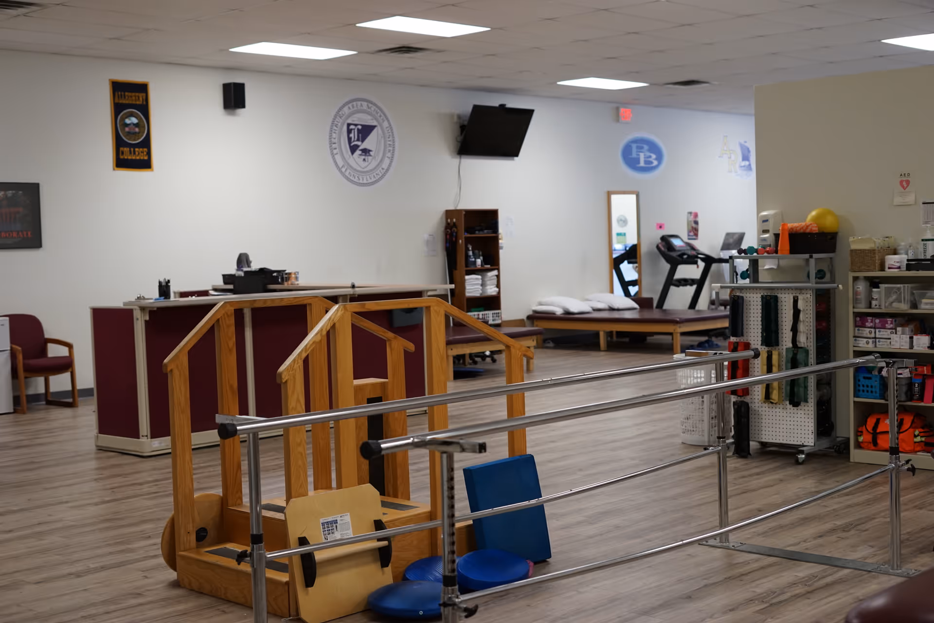Interior therapy gym with parallel bars, exercise equipment, and a reception desk.