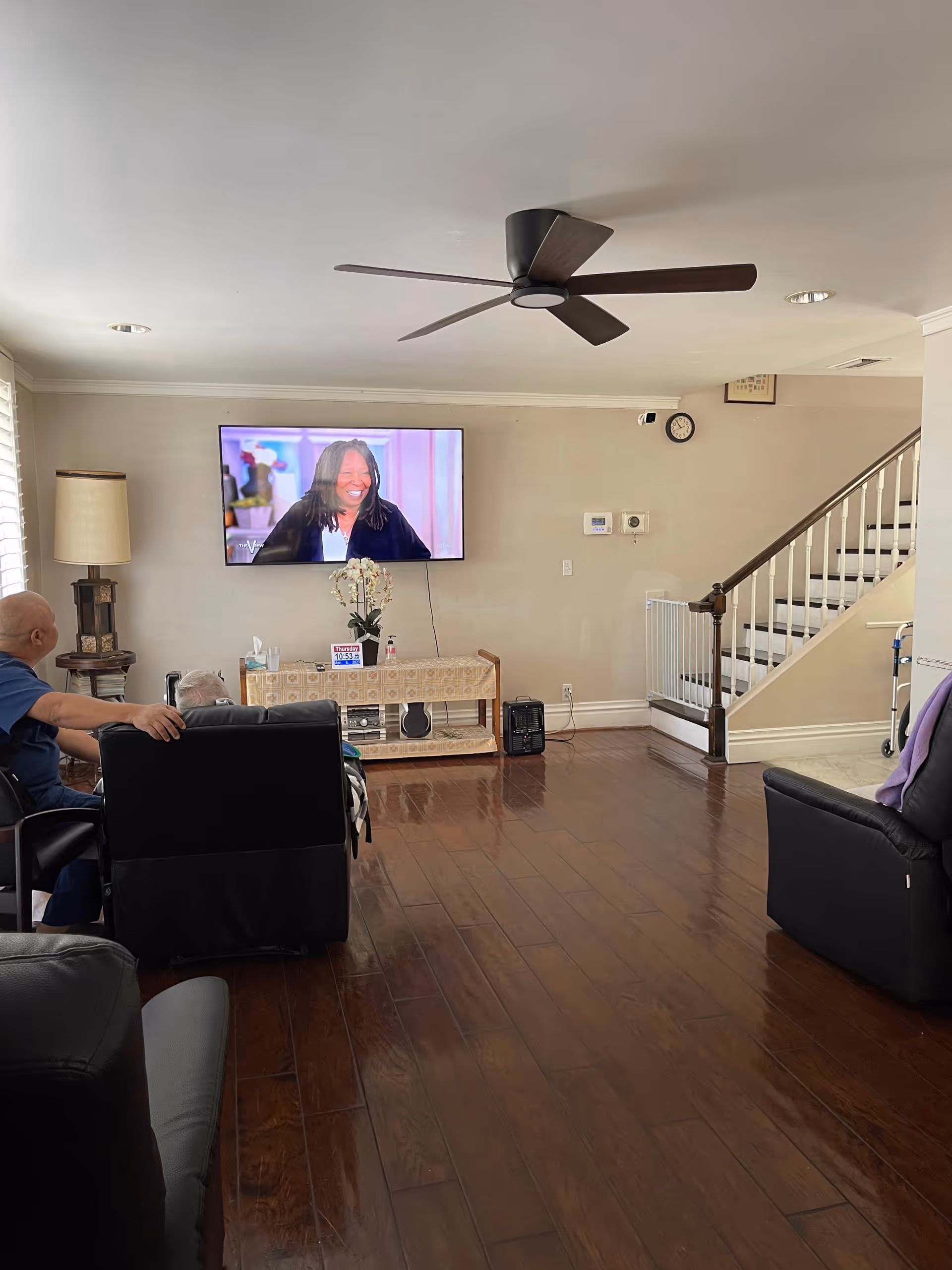 Spacious senior living living room with wall-mounted TV and residents seated in lounge chairs.