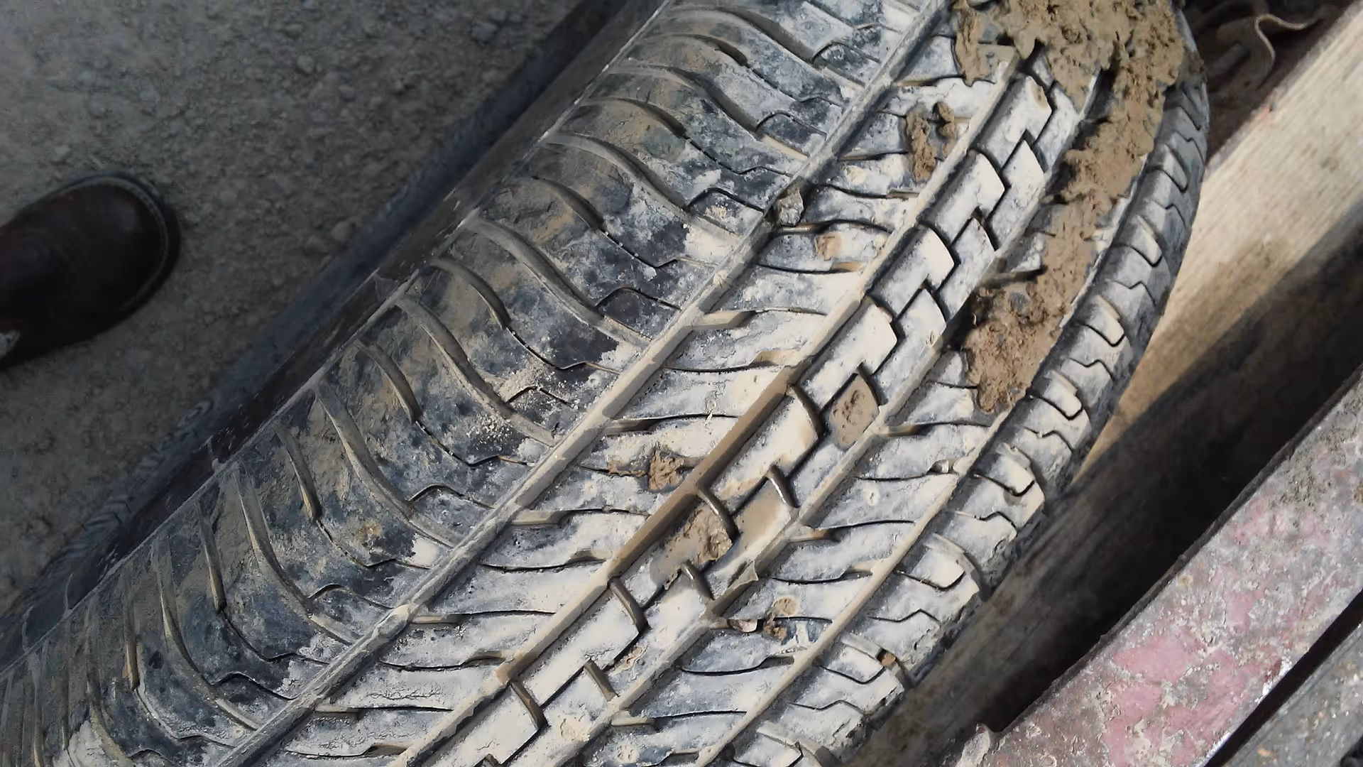Close-up of a muddy tire on dirt with a partial shoe in the corner.