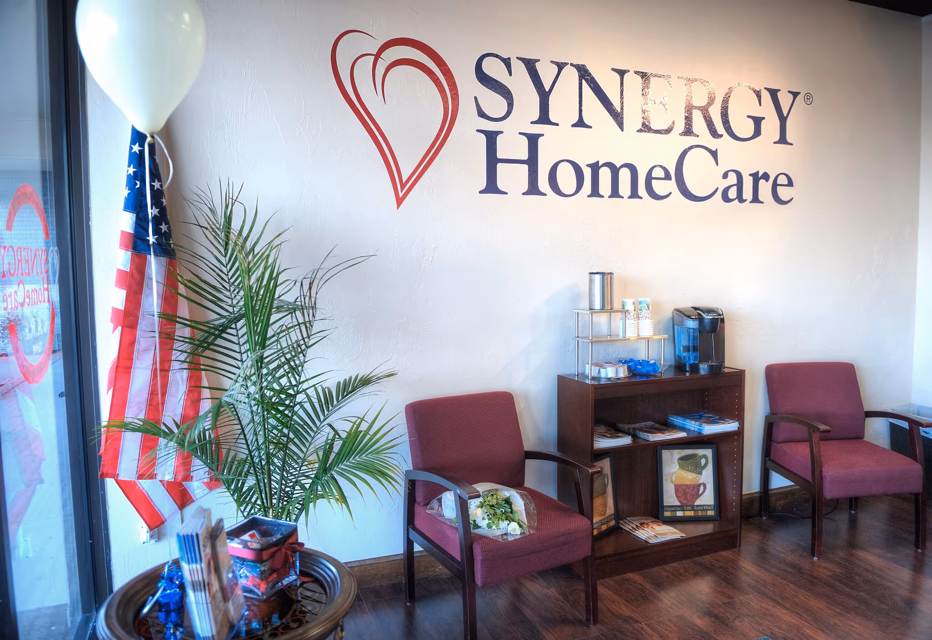 Lobby area with SYNERGY HomeCare sign, chairs, plant, and coffee station.