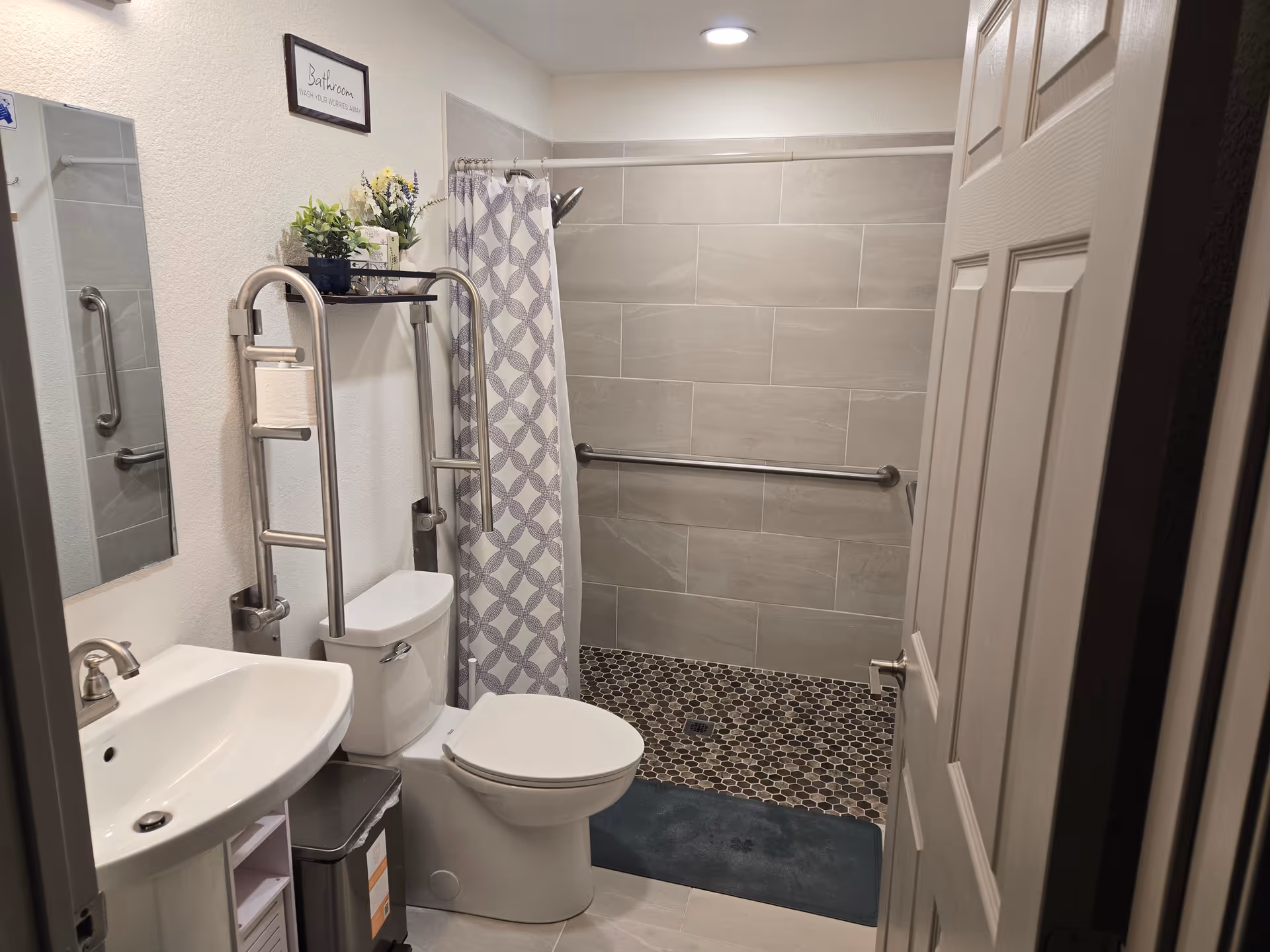 Modern bathroom in senior care facility with toilet, sink, grab bars, and tiled shower.