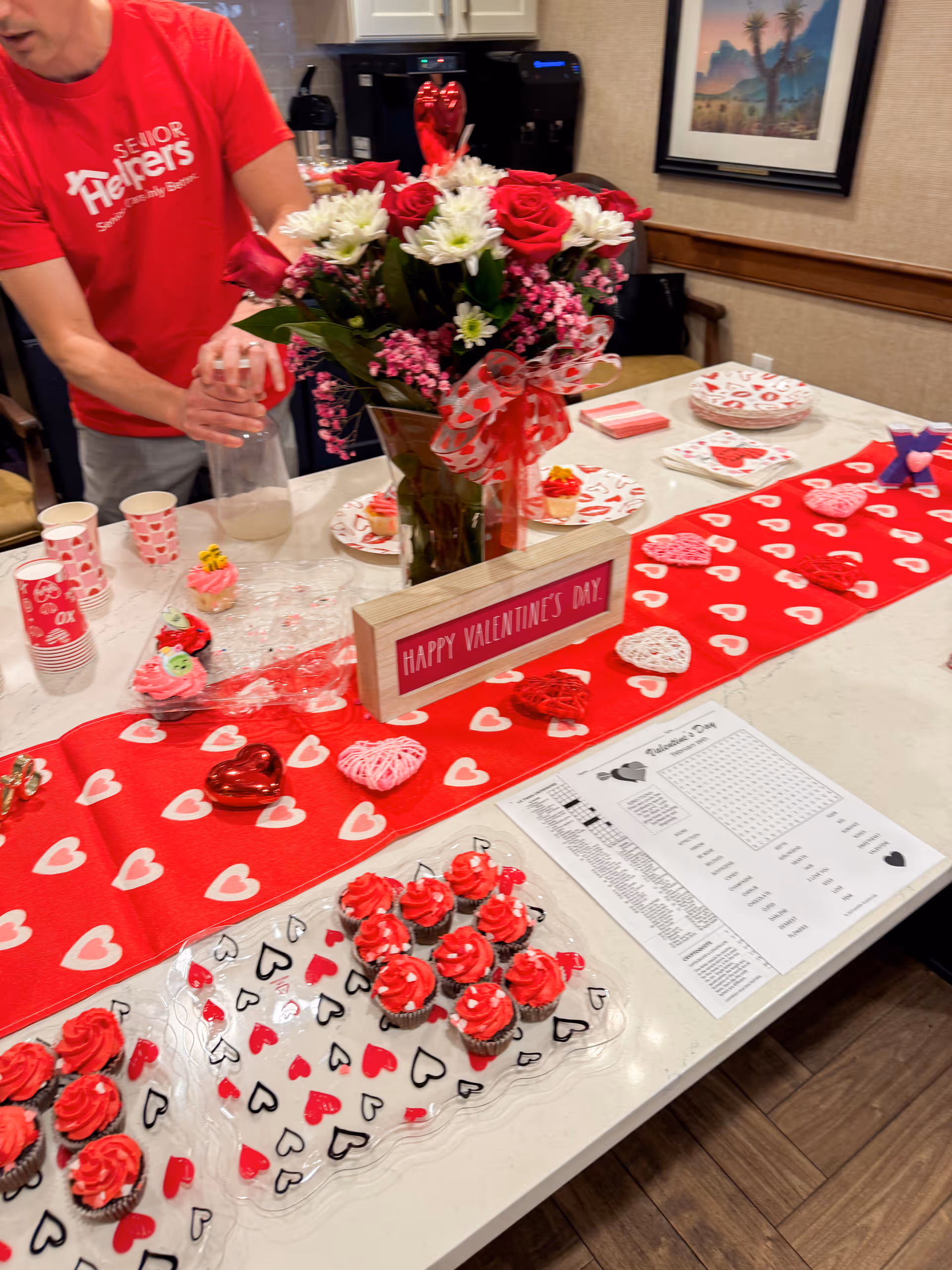 Valentine's Day table setup with cupcakes, flowers, and red decor in a dining area.