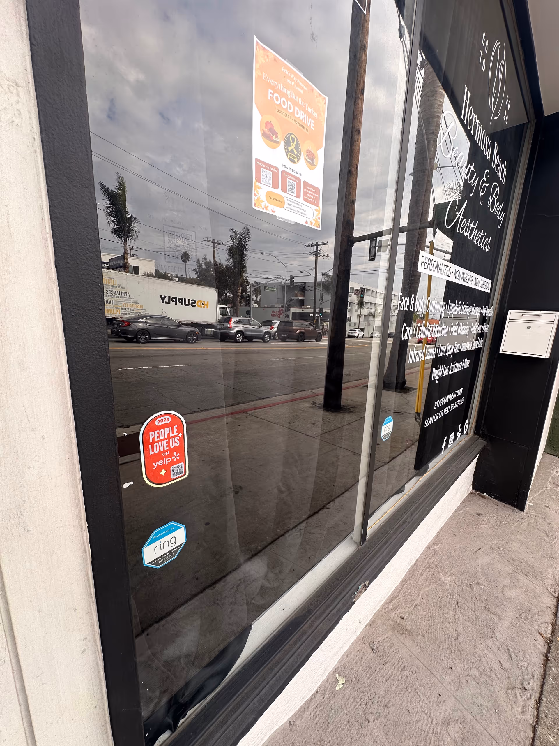 Glass storefront with posters, stickers, and reflections of passing cars on the street.