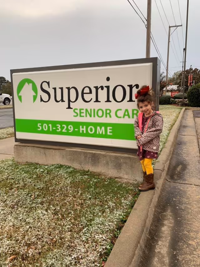 Young child stands beside a large Superior Senior Care sign at a facility entrance.