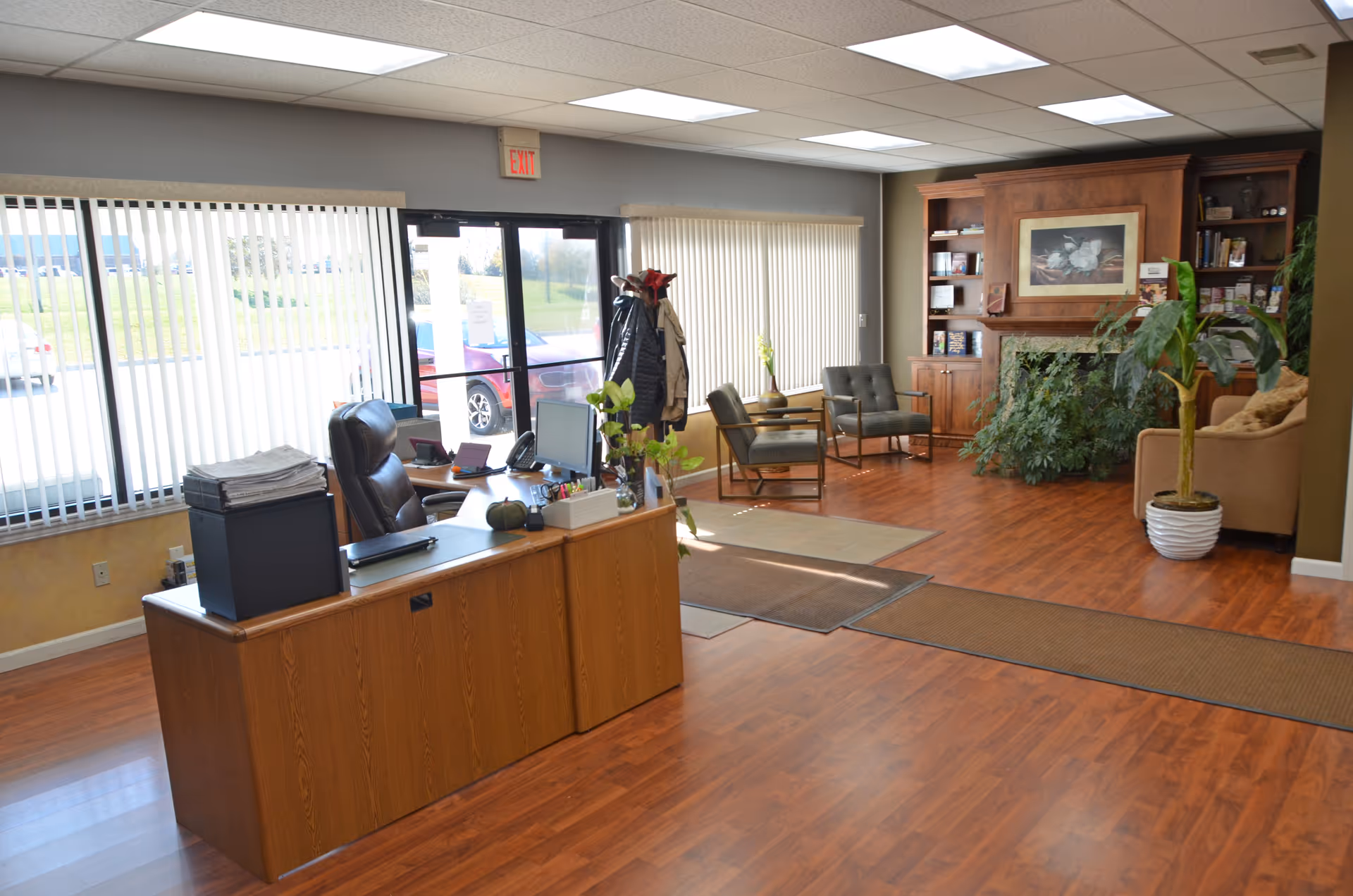 Wooden reception desk in a spacious lobby with seating, plants, and a bookshelf.
