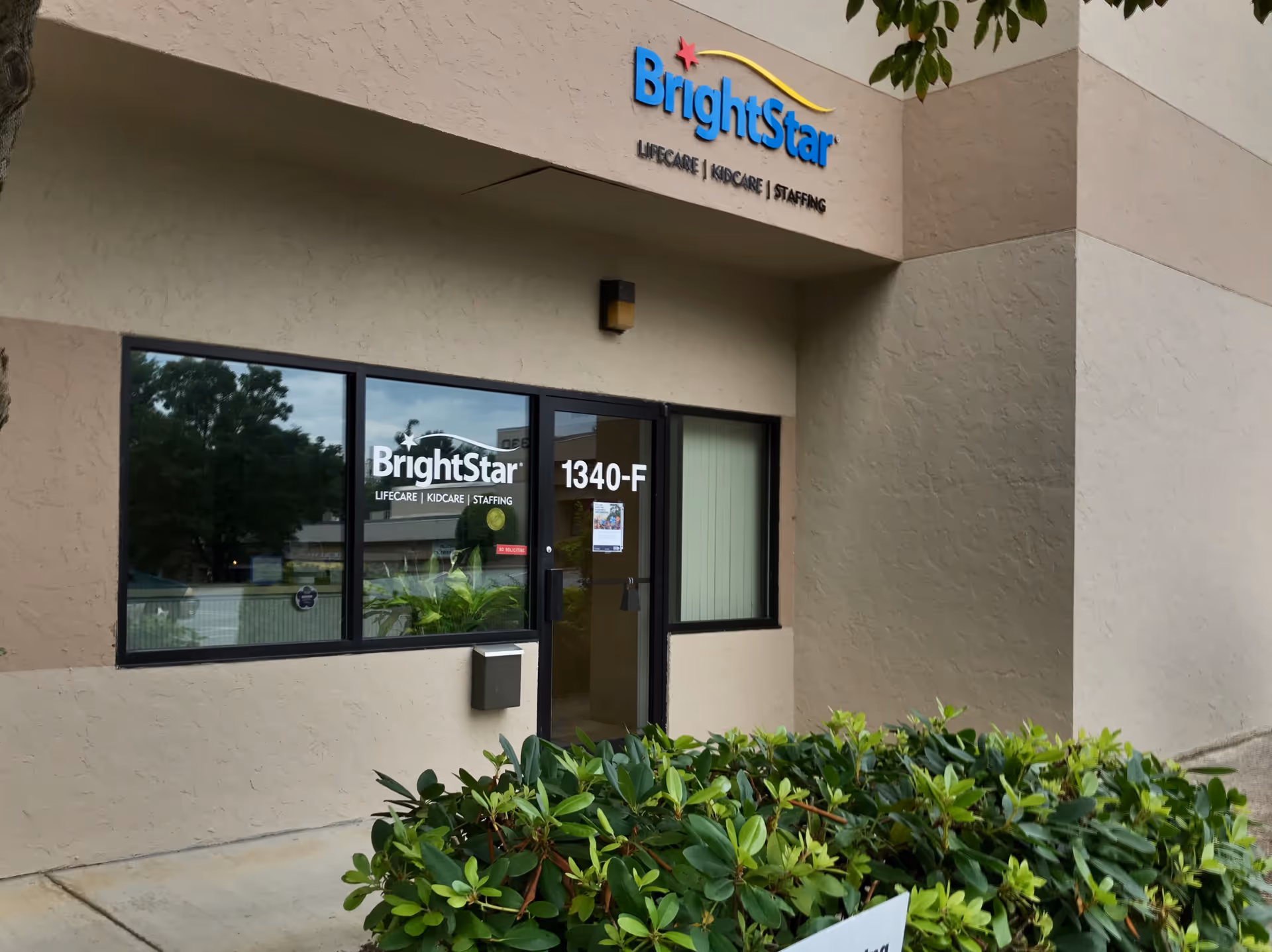 Exterior view of BrightStar Care facility entrance with signage and greenery in front.
