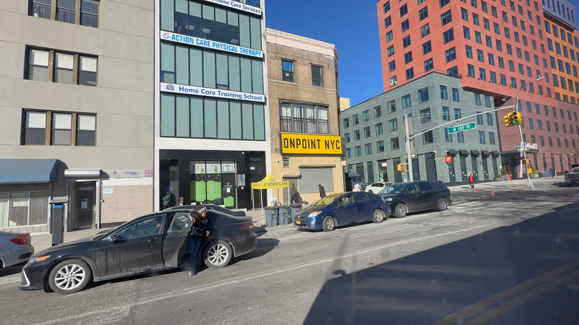 Urban city street with tall buildings, storefronts, and parked cars.
