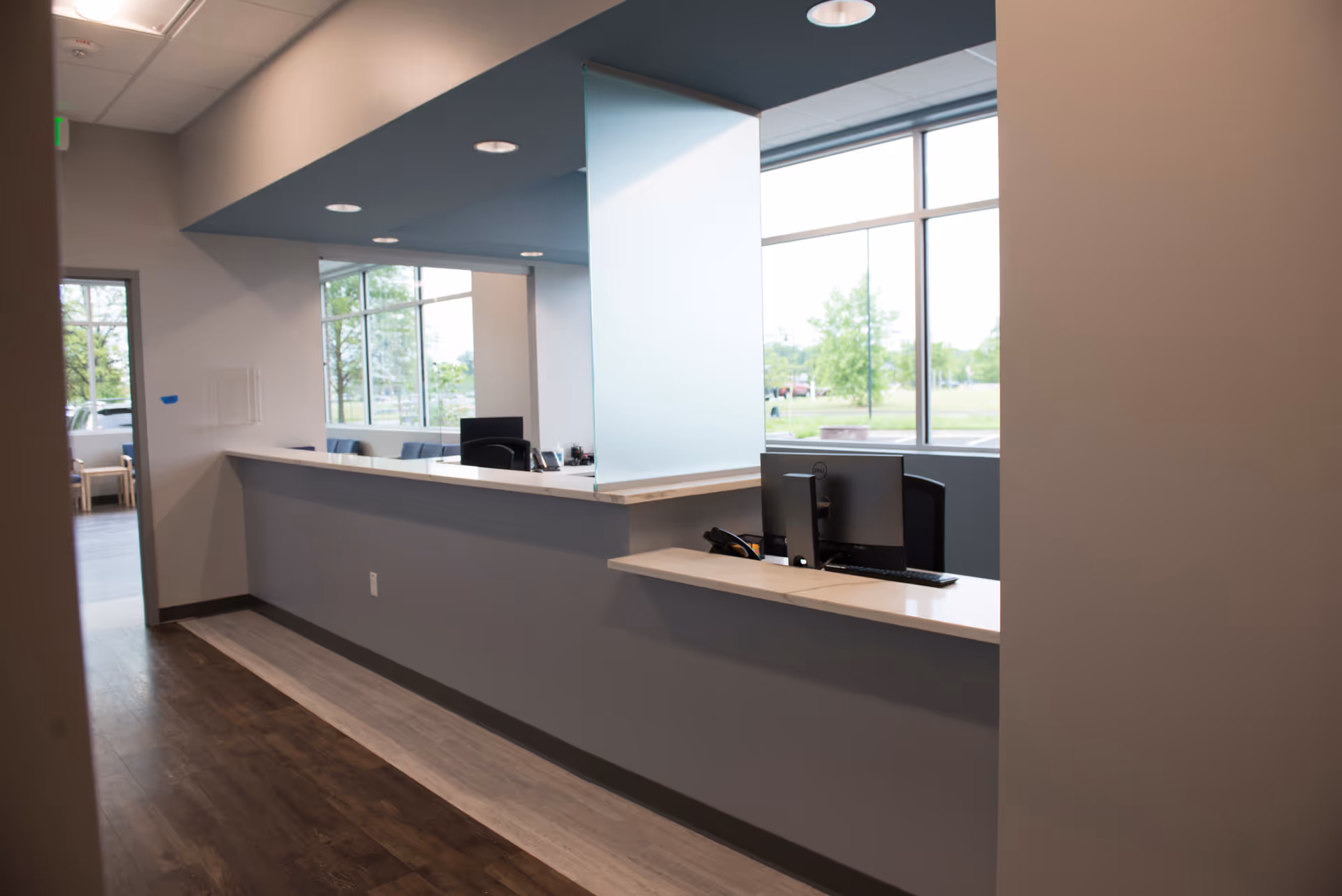 Modern reception area with a long white counter and computers by large windows.