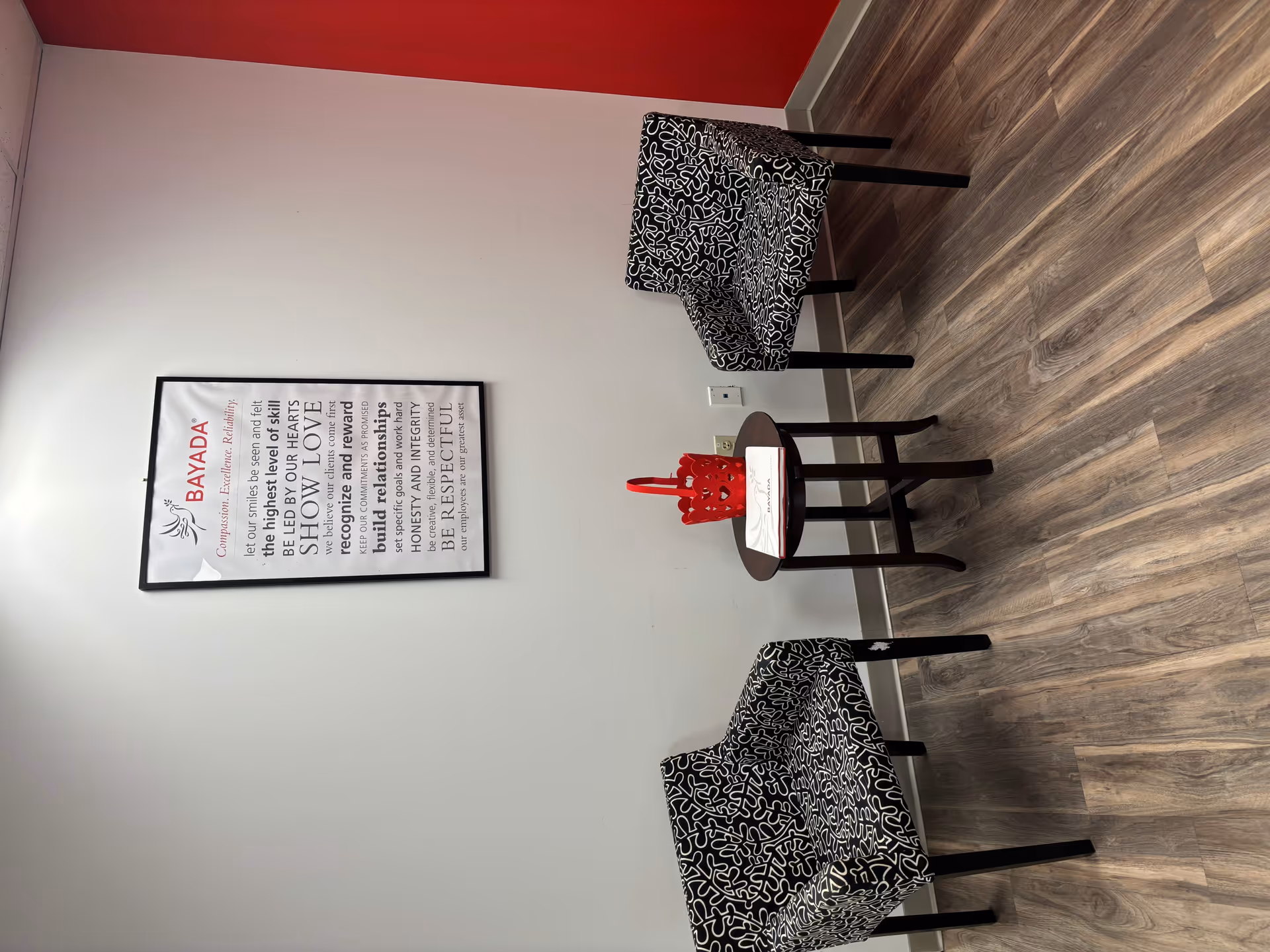 Interior seating area with patterned chairs, a small round table, and BayADA wall art.