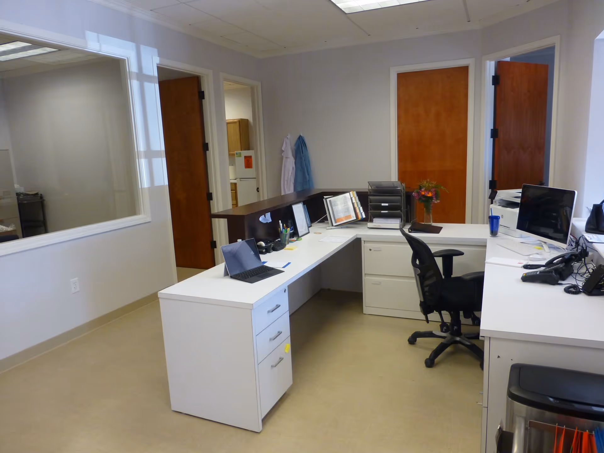 L-shaped desks with computers and office chairs in a clinical reception area