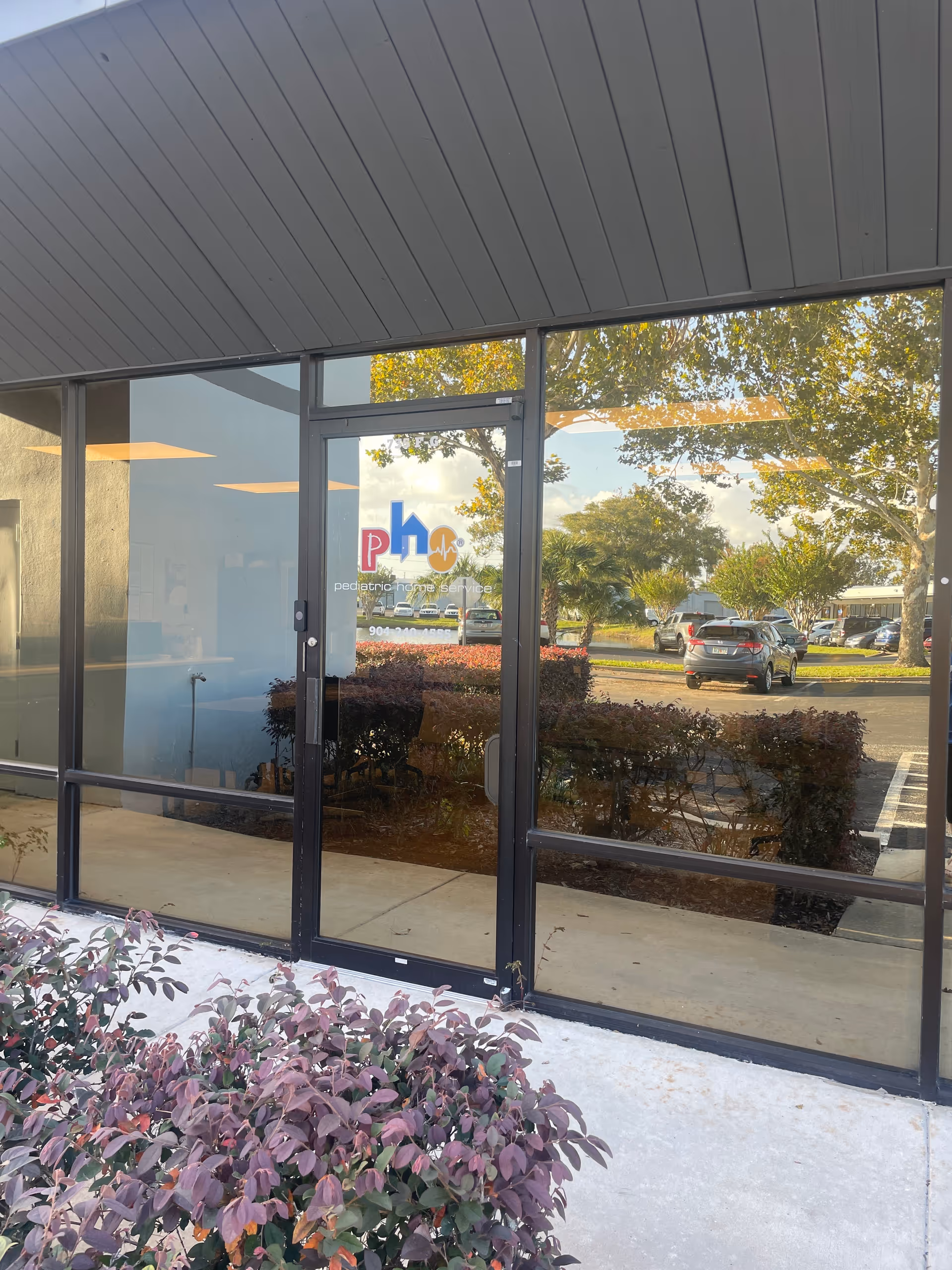 Glass entrance doors with Pediatric Home Service logo and reflections of a parking lot outside.