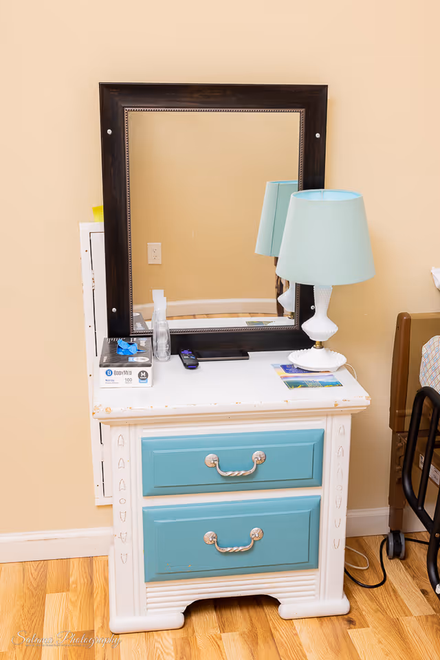 Teal-drawer dresser with a mirror and blue lamp in a bedroom setting.